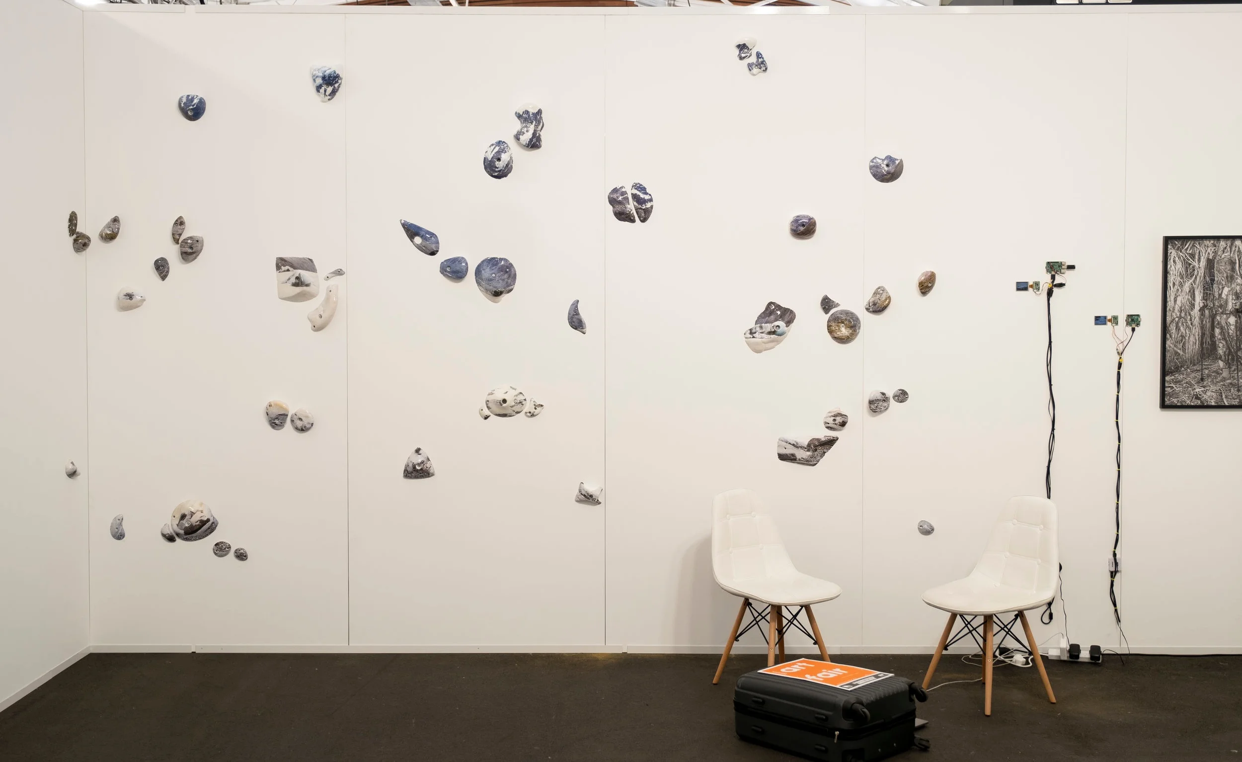 Installation view Michael Bugelli Gallery, Auckland Art Fair. Kai Wasikowski artworks Left-Right: Climb, grip, hold #3 , 2019, hydrographic prints on rock climbing holds, dimensions variable. Streaming #4 , 2017, single channel video (5m 18s loop), LCD display, RaspberryPi, HDMI and component cables, 9 x 4 cm display, dimensions variable. 10 January 2017 #3 , 2017, single channel video (4m 29s loop), LCD display, RaspberryPi, HDMI and component cables, 7 x 3 cm display, dimensions variable. Garden #2 , 2019, inkjet print on cotton rag, 77 x 60 cm. Image: Josef Scott.