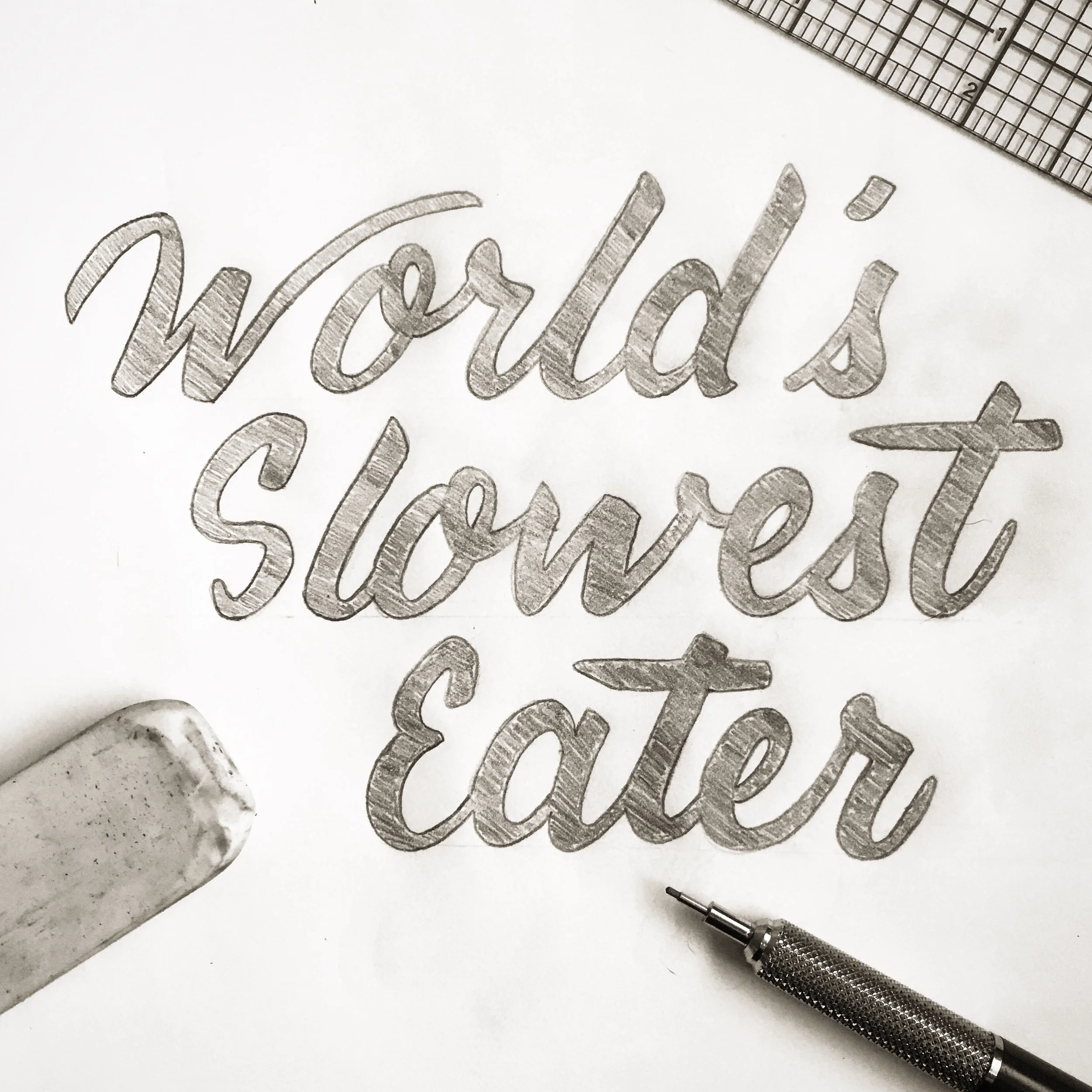 Handlettered words on paper reads 'World's Slowest Eater' with a pencil and eraser nearby. 