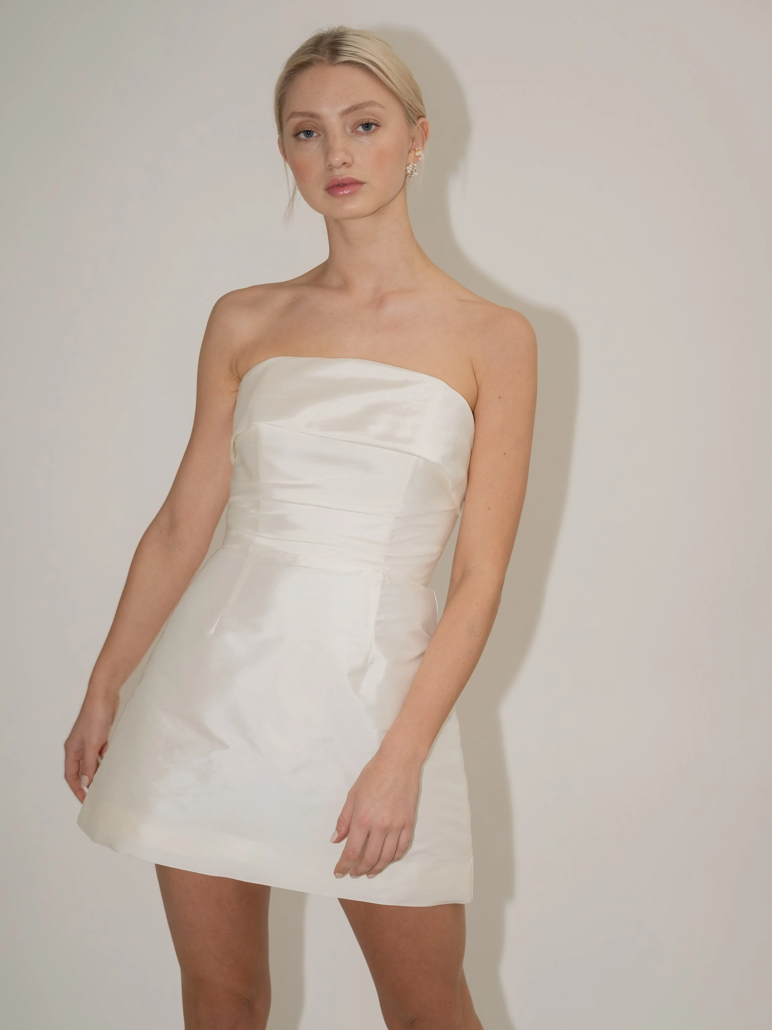 A move on from our best-selling Alexa style with a softer more romantic finish. Constructed in Ivory taffeta, this gown features a fully boned bodice with bias draped neckline and ruches that hug the waist. This is paired with our signature mini A-li
