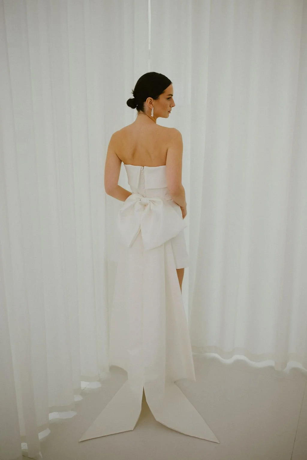 For brides seeking even greater drama, the Stace Bow Train offers an elevated evolution of our signature Alexa Bow. Crafted from structured Mikado, its oversized bow and elongated tails create a graceful train and striking architectural silhouette. D
