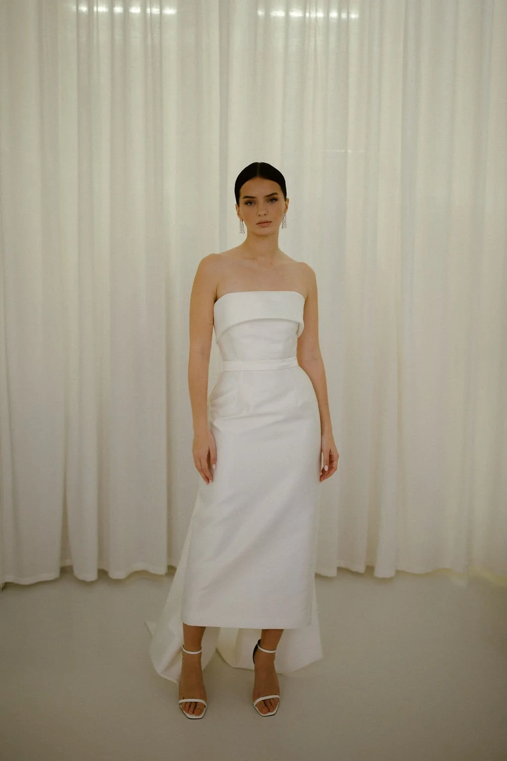 Effortlessly elegant, the Alexa Midi is a modern bridal silhouette crafted in our signature Mikado. A supportive boned internal bodice and refined bias band neckline create a beautifully structured fit, while the sleek column skirt offers clean, unde