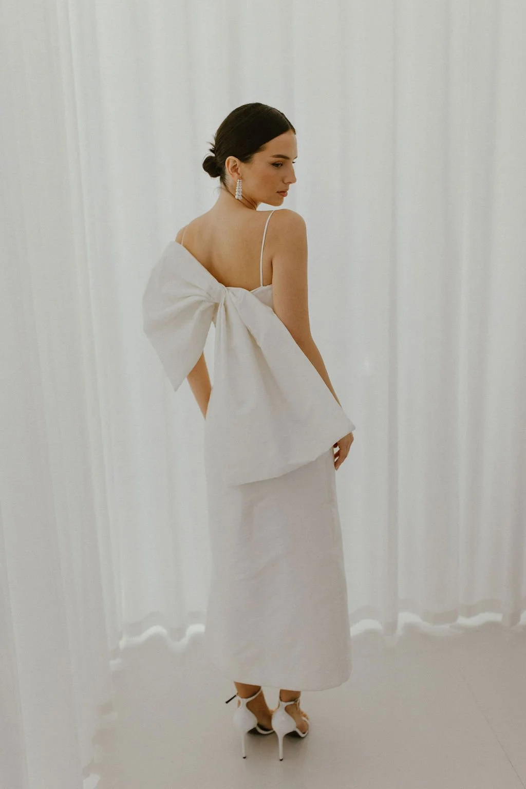 The perfect reception or civil ceremony piece. The She Midi features side waist pleating, an above ankle hemline and side split. Style alone or layer with our sleeve / bow additions for an interchangeable look. Fastens with concealed side zip allowin