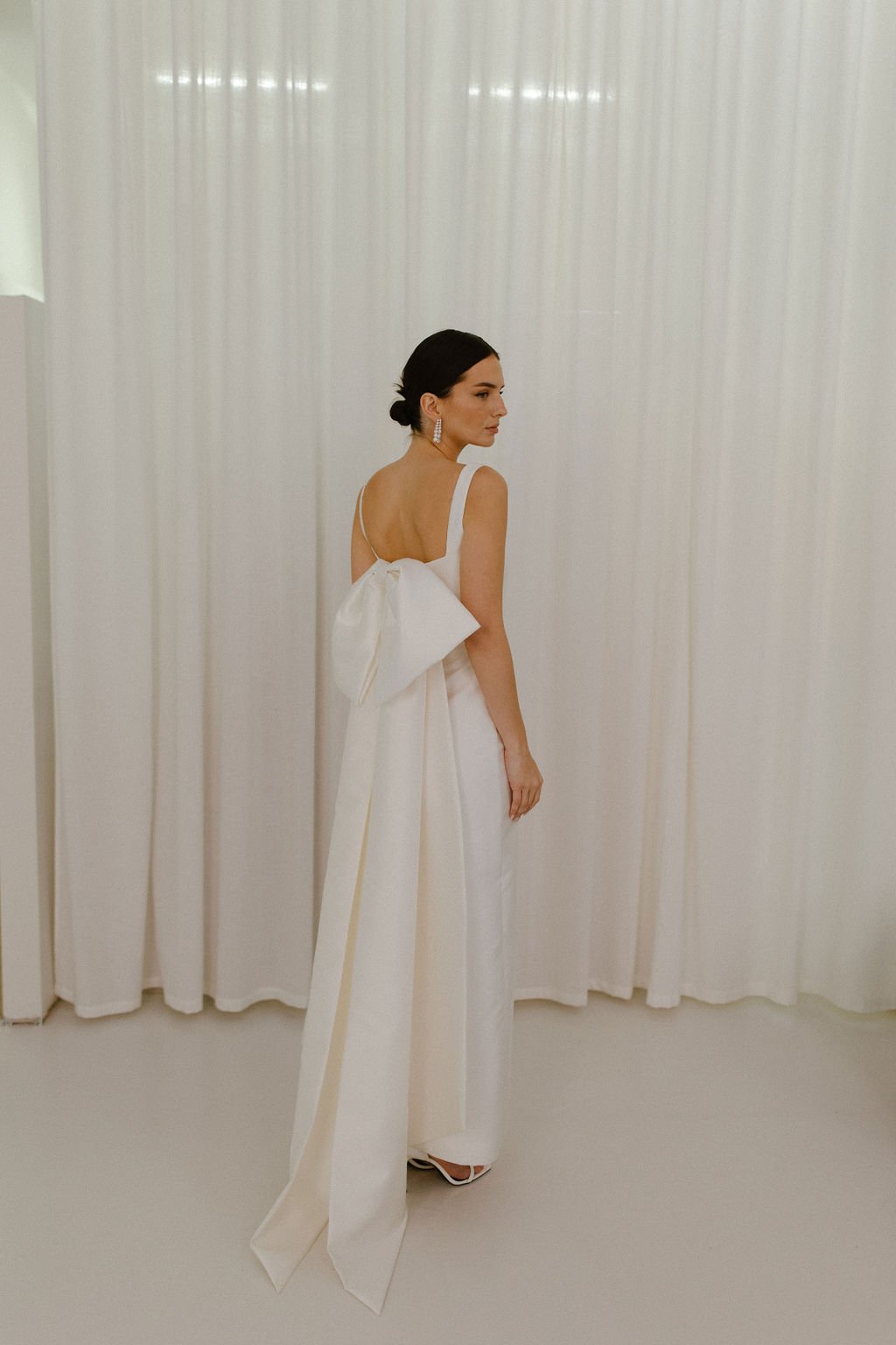 For brides seeking even greater drama, the Stace Bow Train offers an elevated evolution of our signature Alexa Bow. Crafted from structured Mikado, its oversized bow and elongated tails create a graceful train and striking architectural silhouette. D