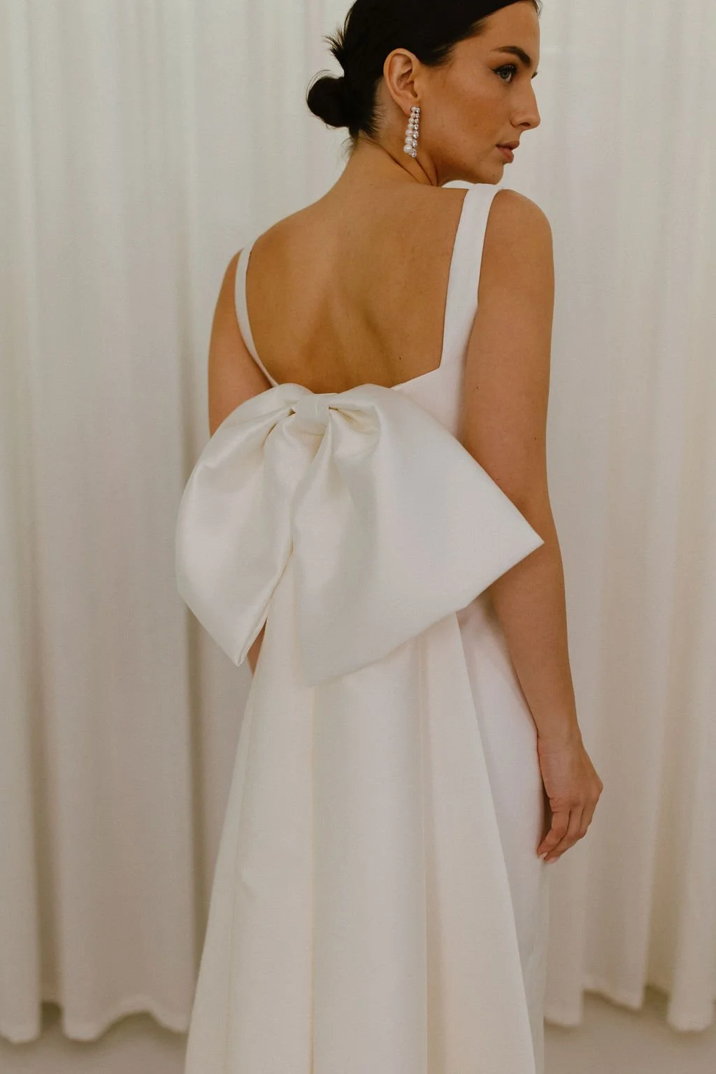 For brides seeking even greater drama, the Stace Bow Train offers an elevated evolution of our signature Alexa Bow. Crafted from structured Mikado, its oversized bow and elongated tails create a graceful train and striking architectural silhouette. D