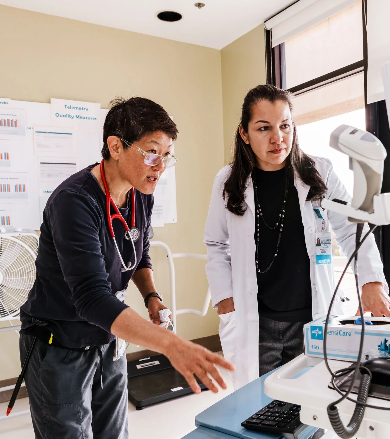 A candid, documentary-style photograph showcasing a hospital clinical team collaborating on patient care in a medical setting. Photography by Carolyn Fong for Flight Design Co.