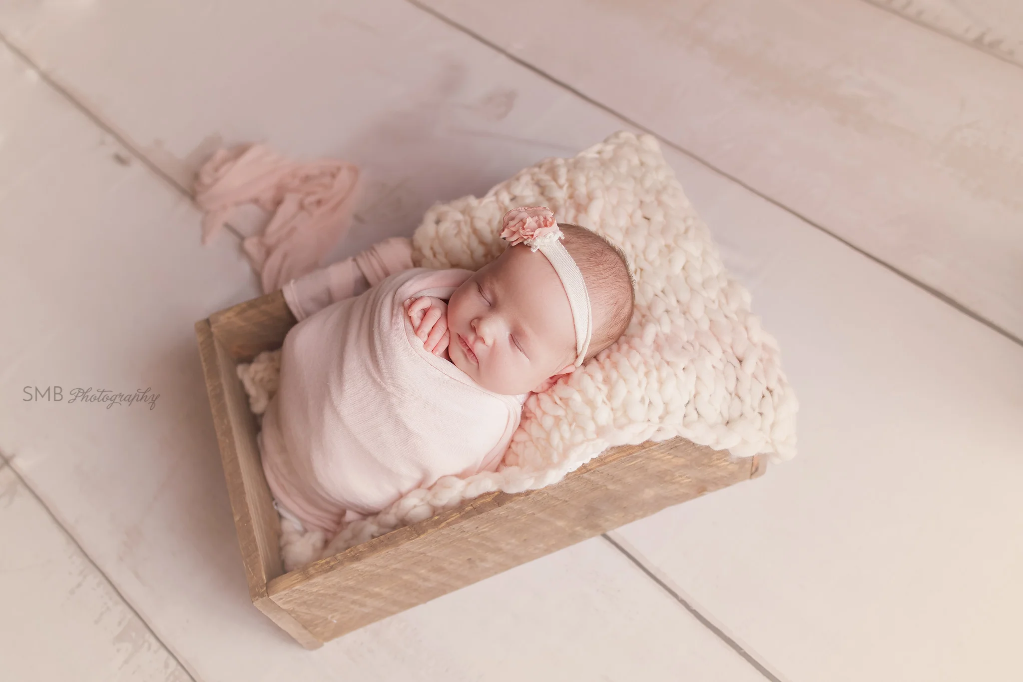 Newborn girl wrapped in pink on cream wood floor
