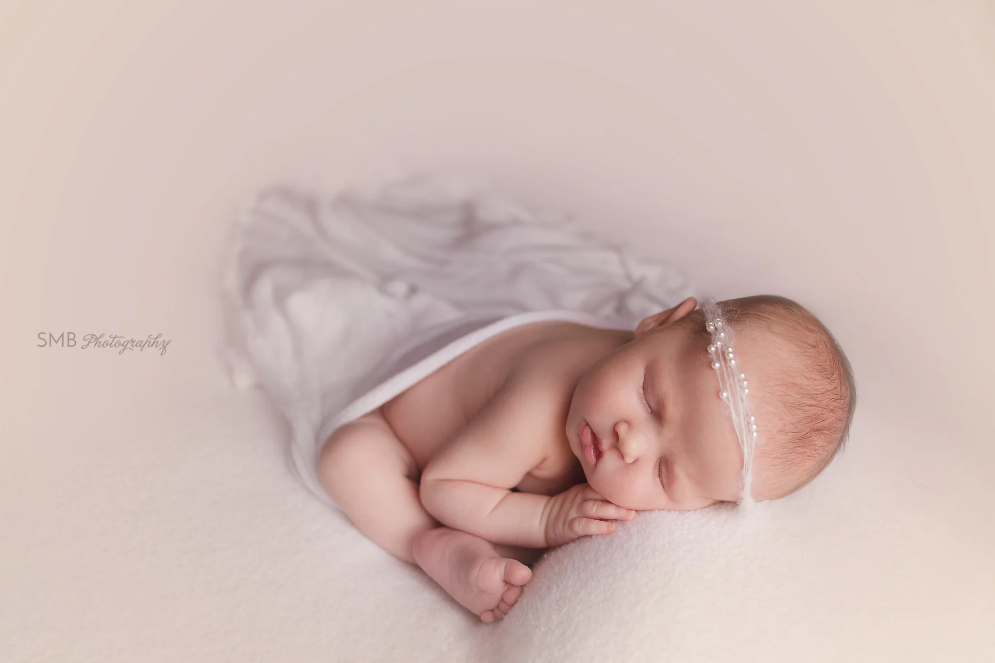 Newborn girl wrapped on fuzzy blanket, wearing pearl headband