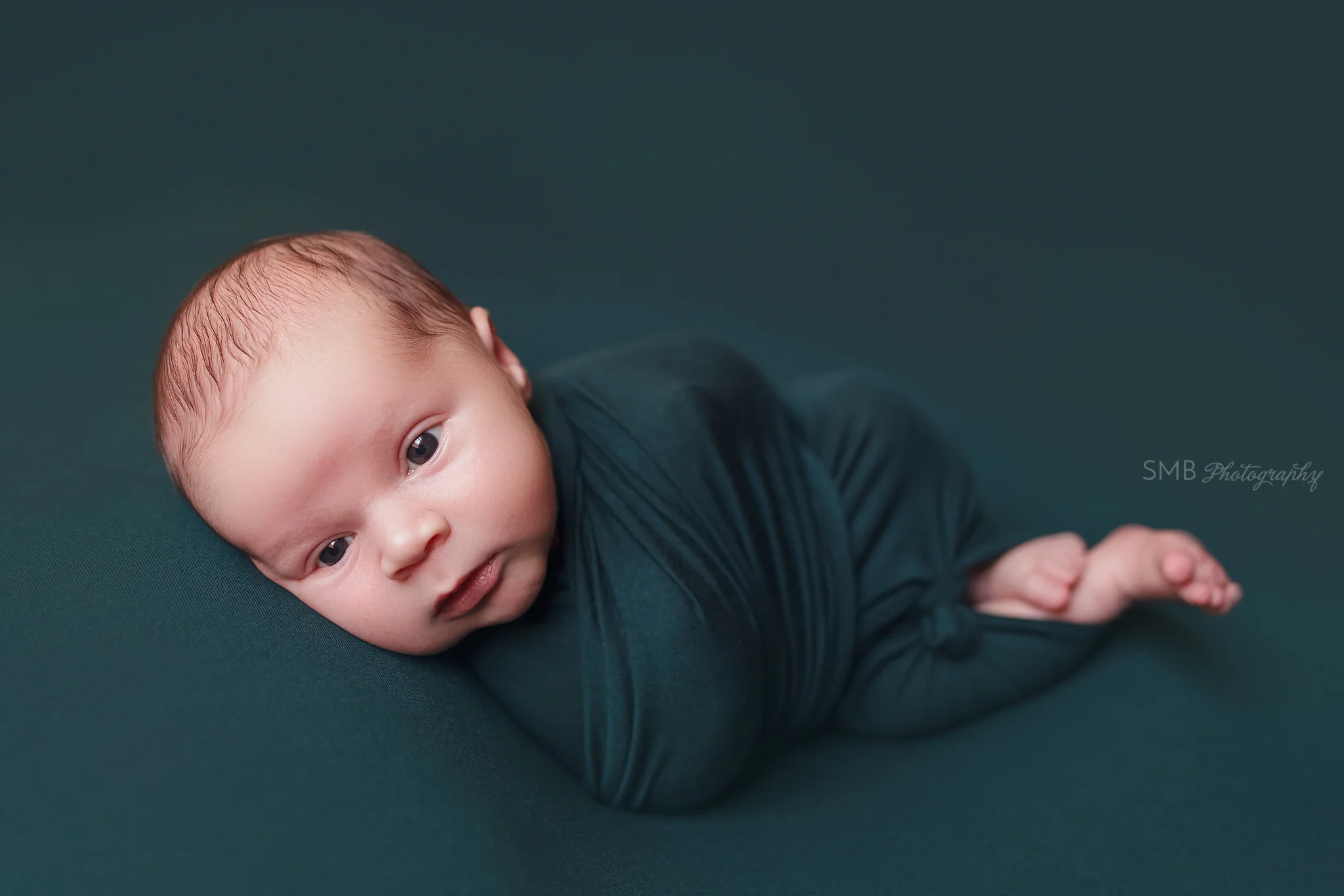 Newborn wrapped on hunter green looking at camera