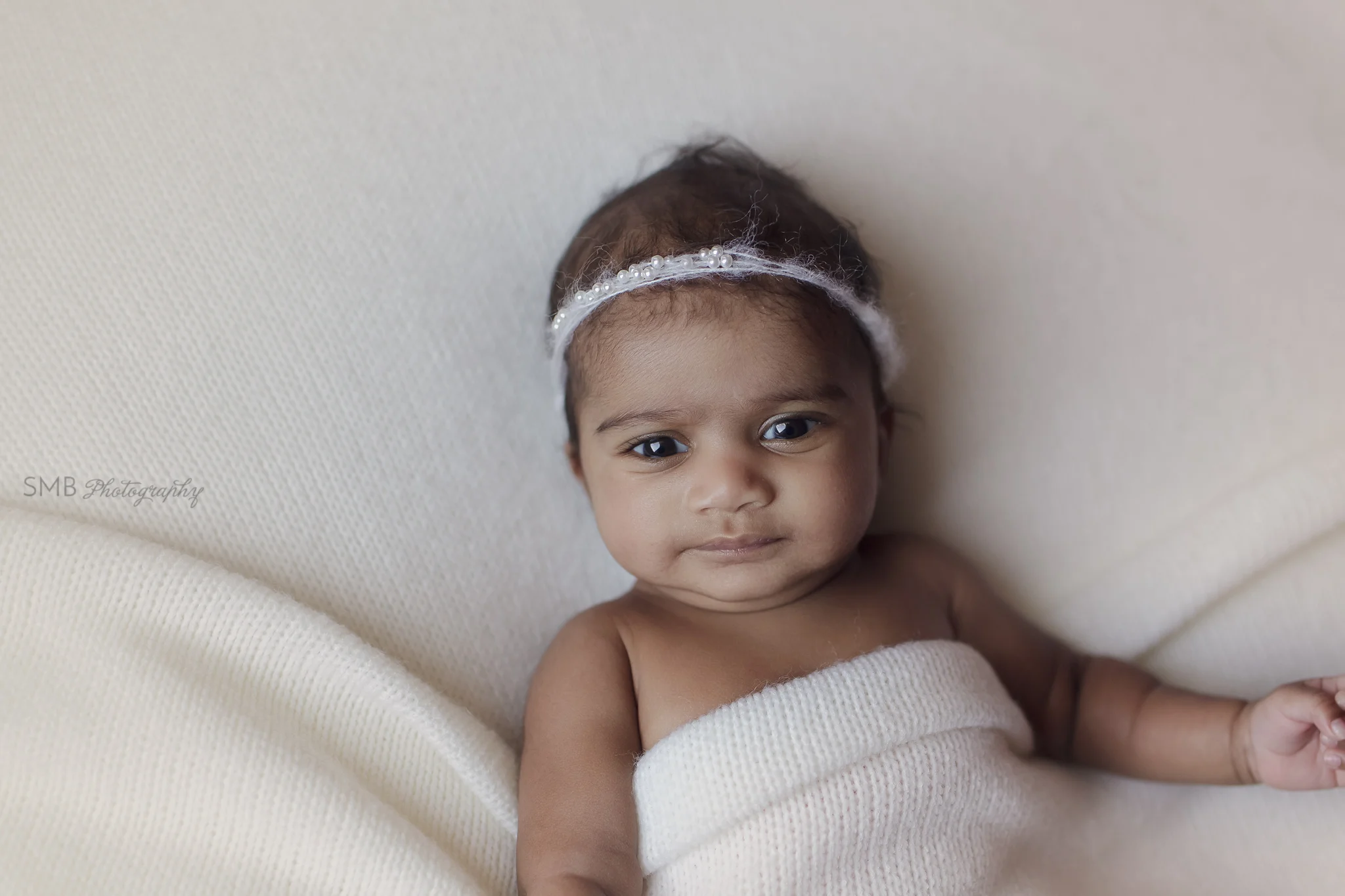 Newborn girl laying on ivory blanket, wearing pearl headband