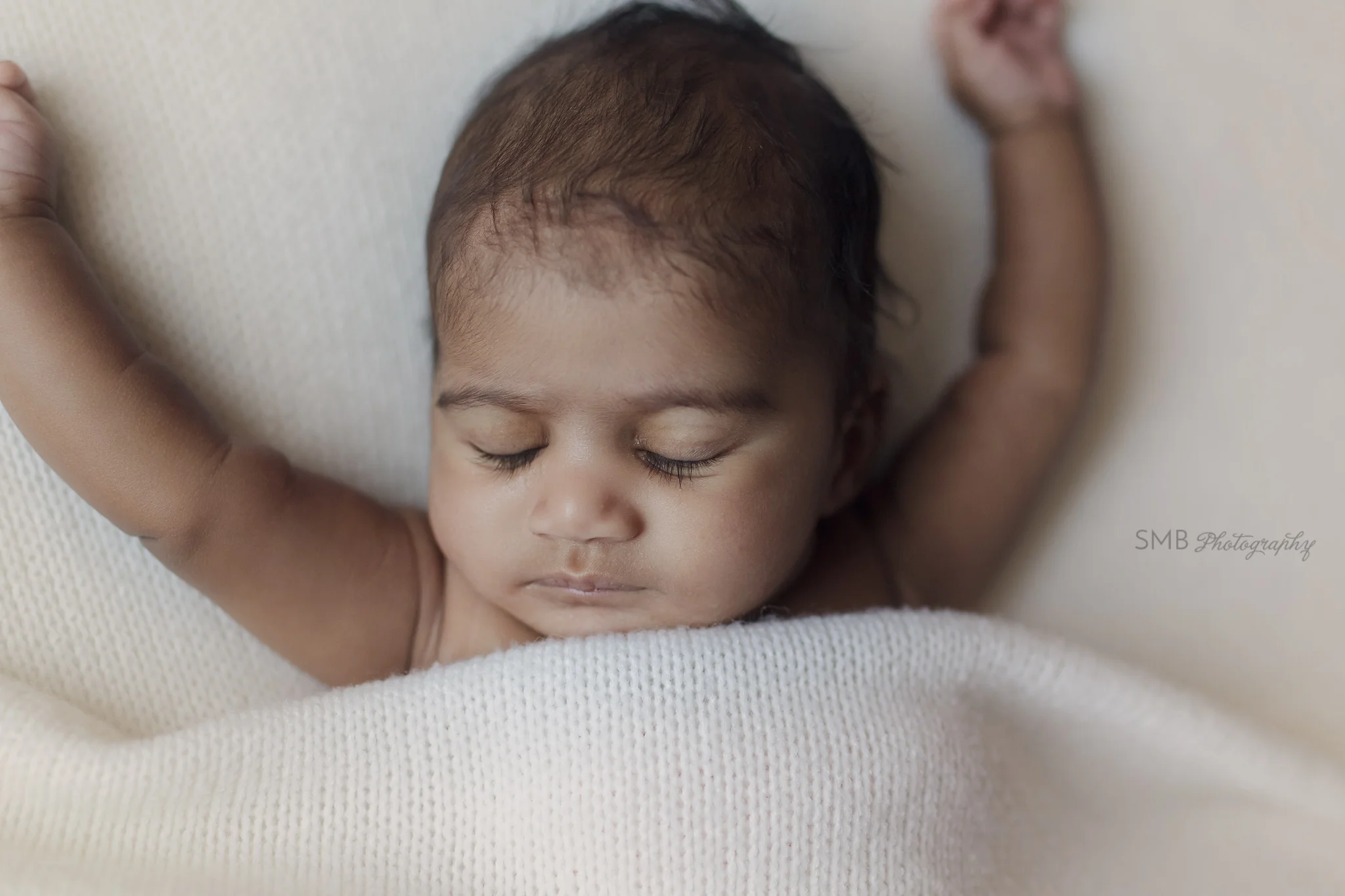 Newborn baby girl sleeping on ivory blanket with arms stretched out