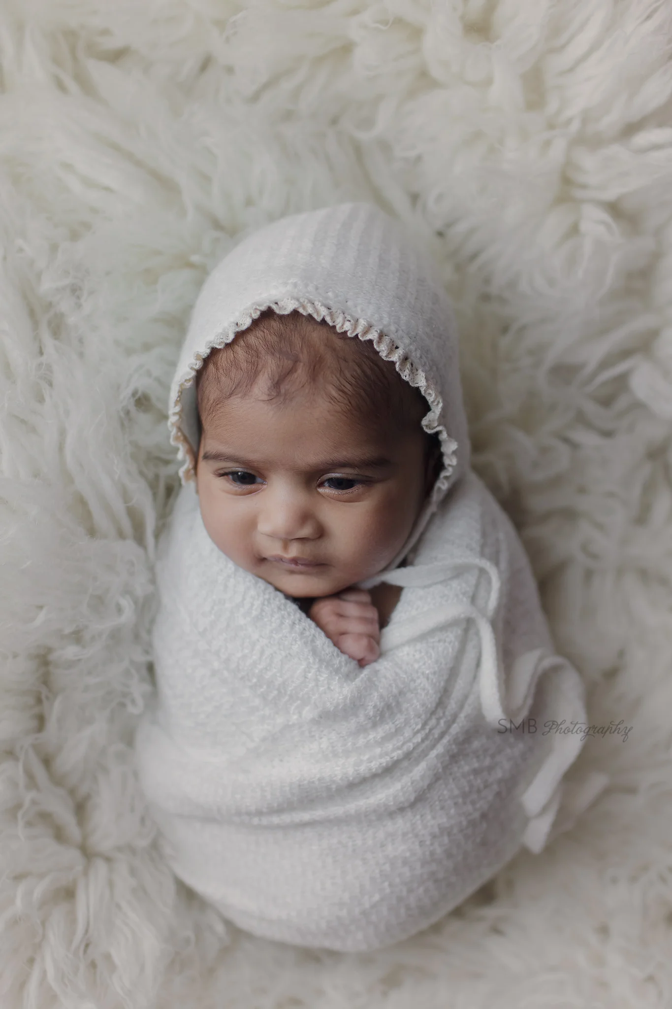Newborn girl wrapped up on white flokati