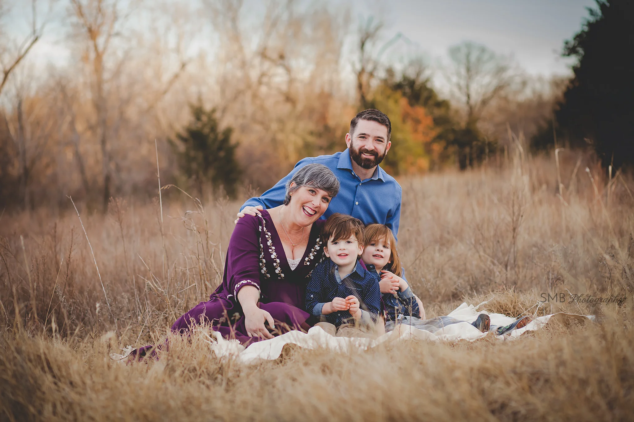 Family smiling looking at camera sitting in a field