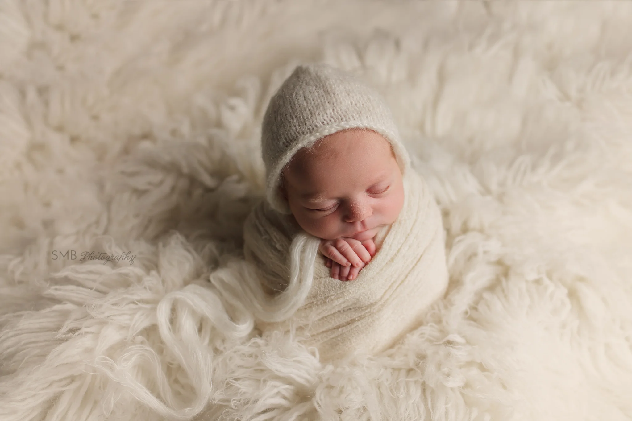 Newborn girl wrapped on cream flokati