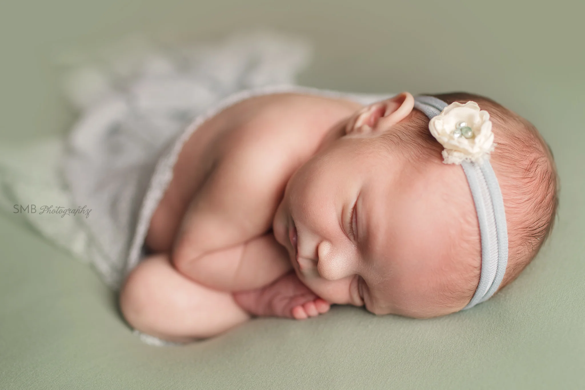 Newborn girl curled up on sage green blanket