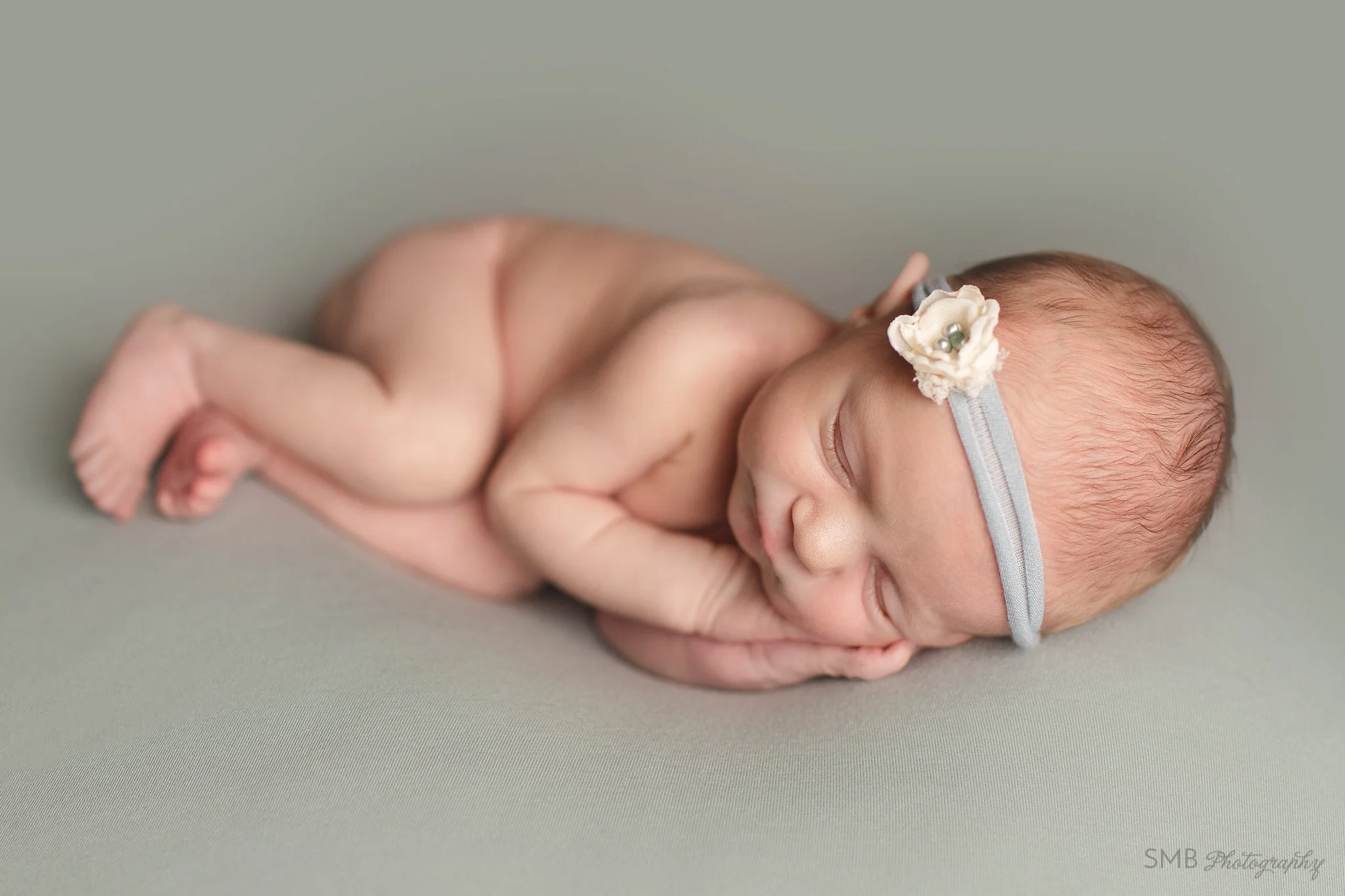 Newborn girl sleeping on greenish blanket with hands under her cheek