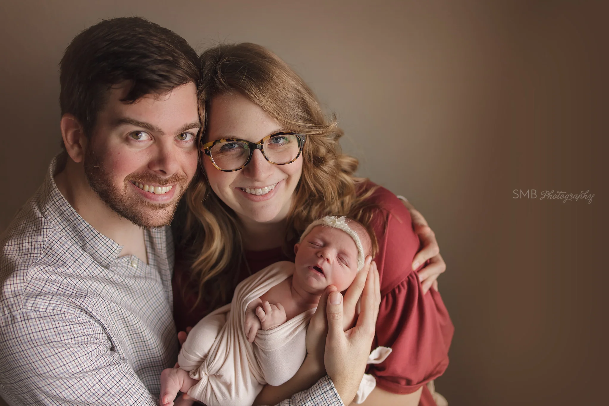 Mom Dad and newborn daughter smiling at camera
