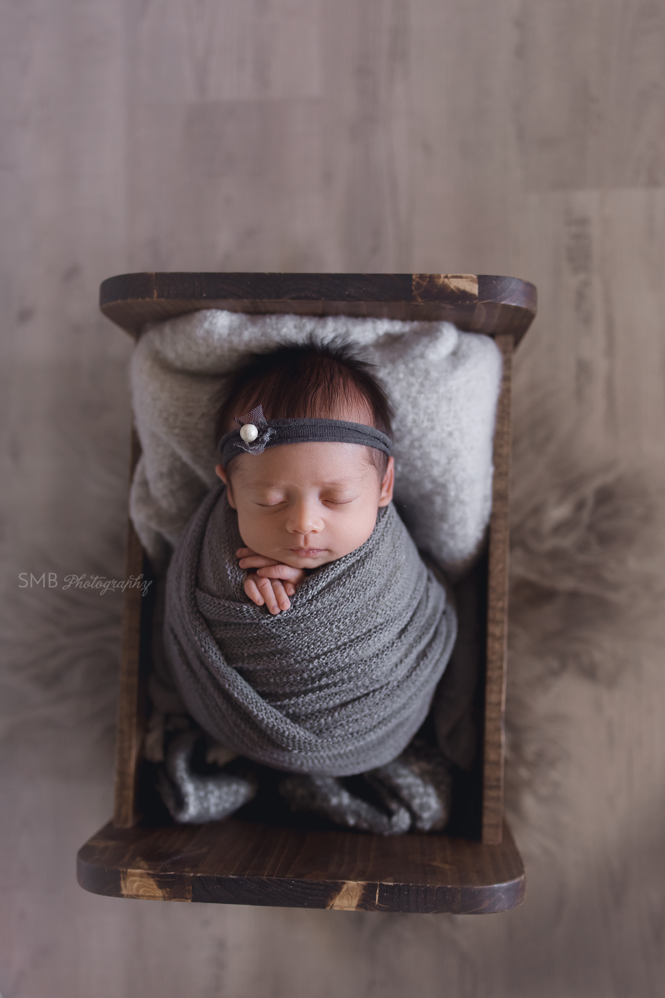 Newborn girl wrapped in gray in baby bed