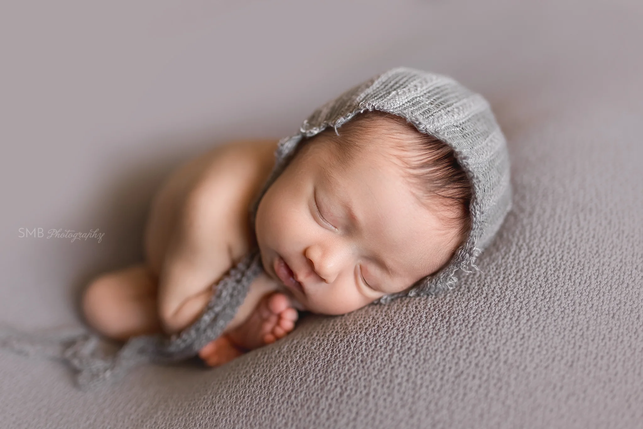 Baby girl on gray blanket wearing gray bonnet