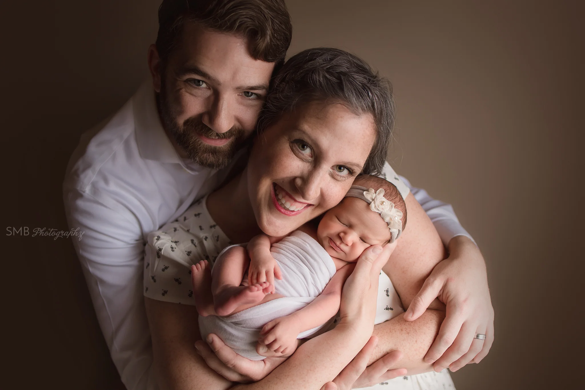 Mom& Dad holding newborn daughter smiling
