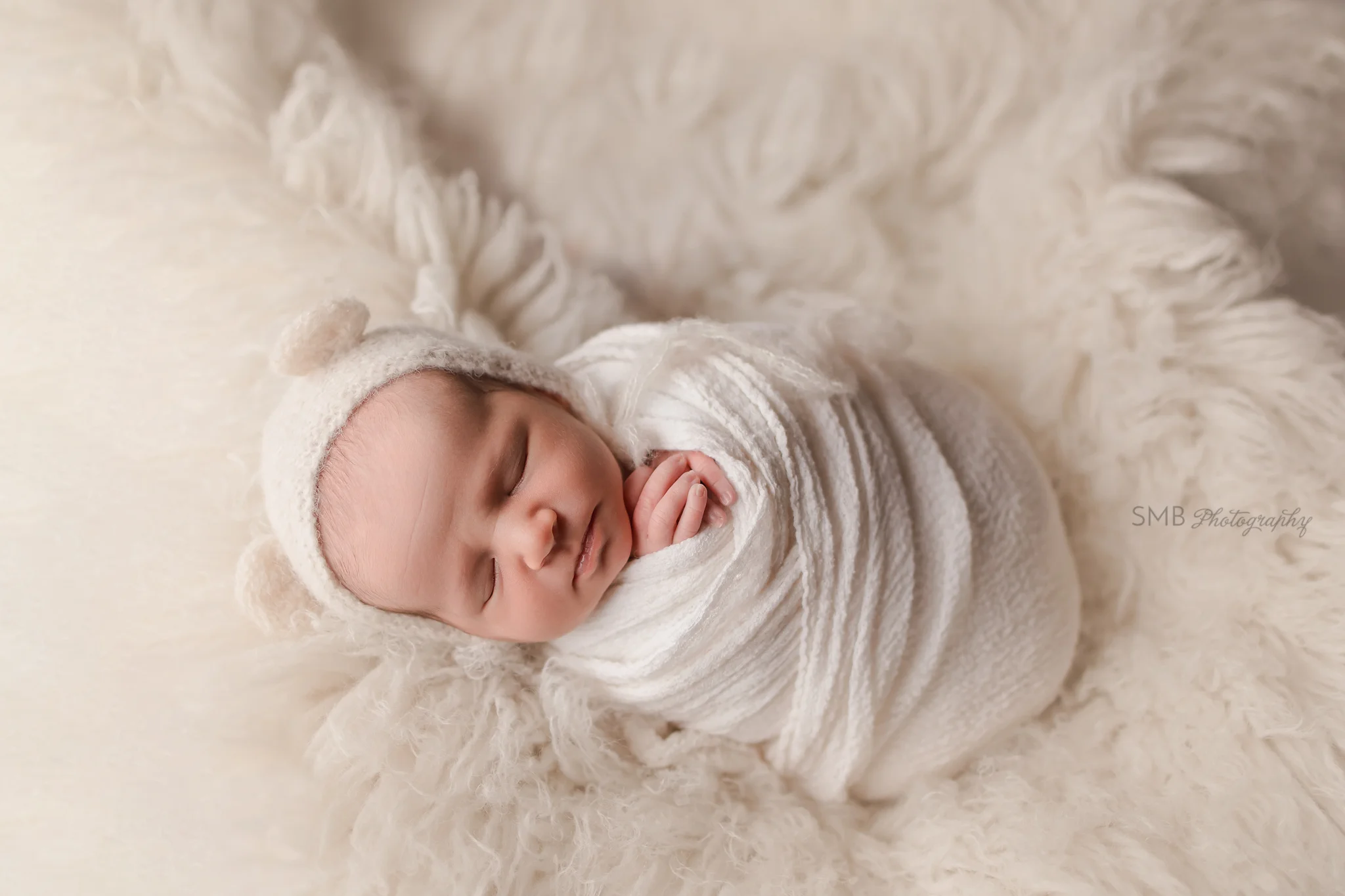 Newborn girl wrapped laying on white flokati