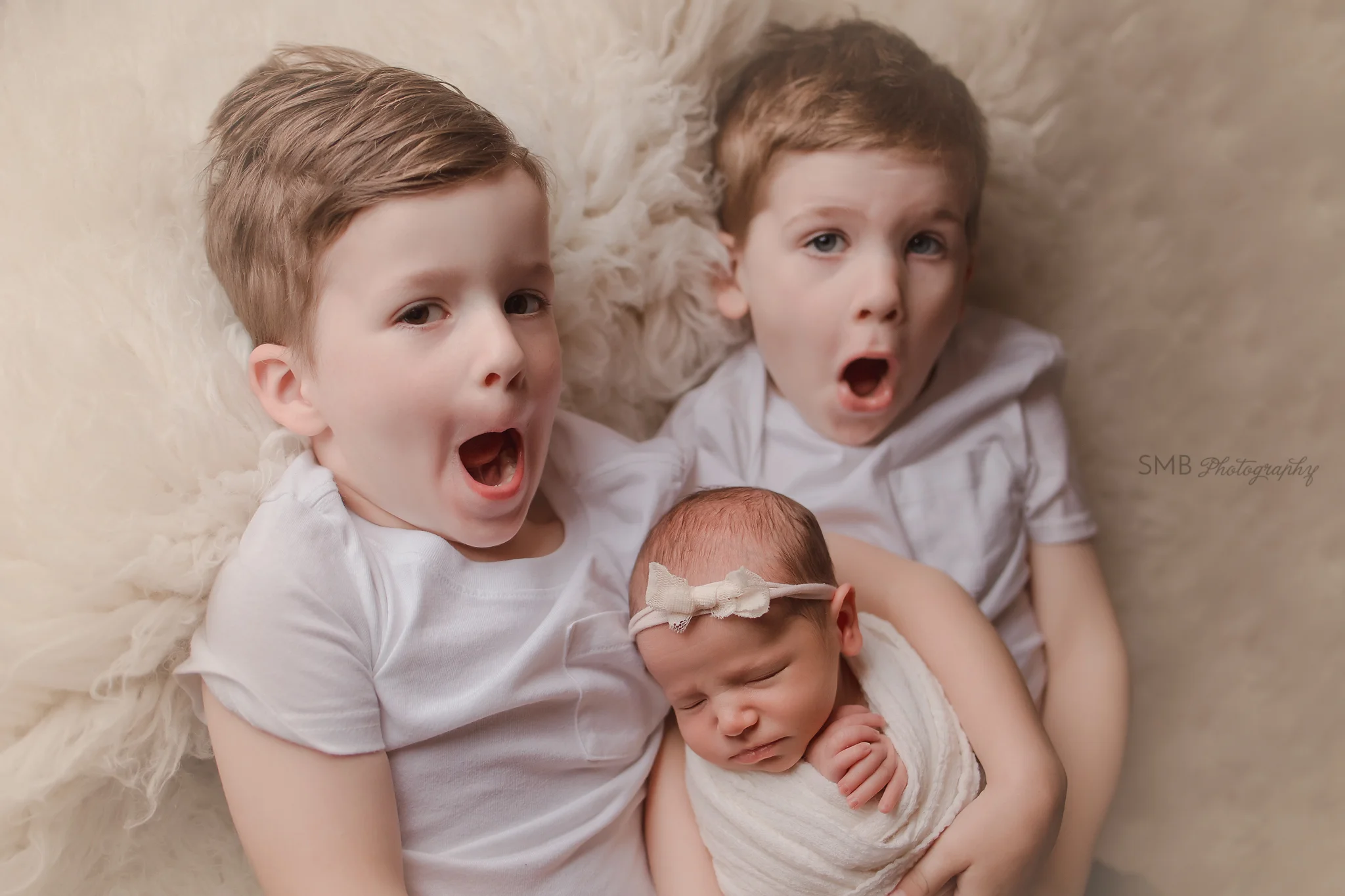 Big brothers holding little sister on white flokati