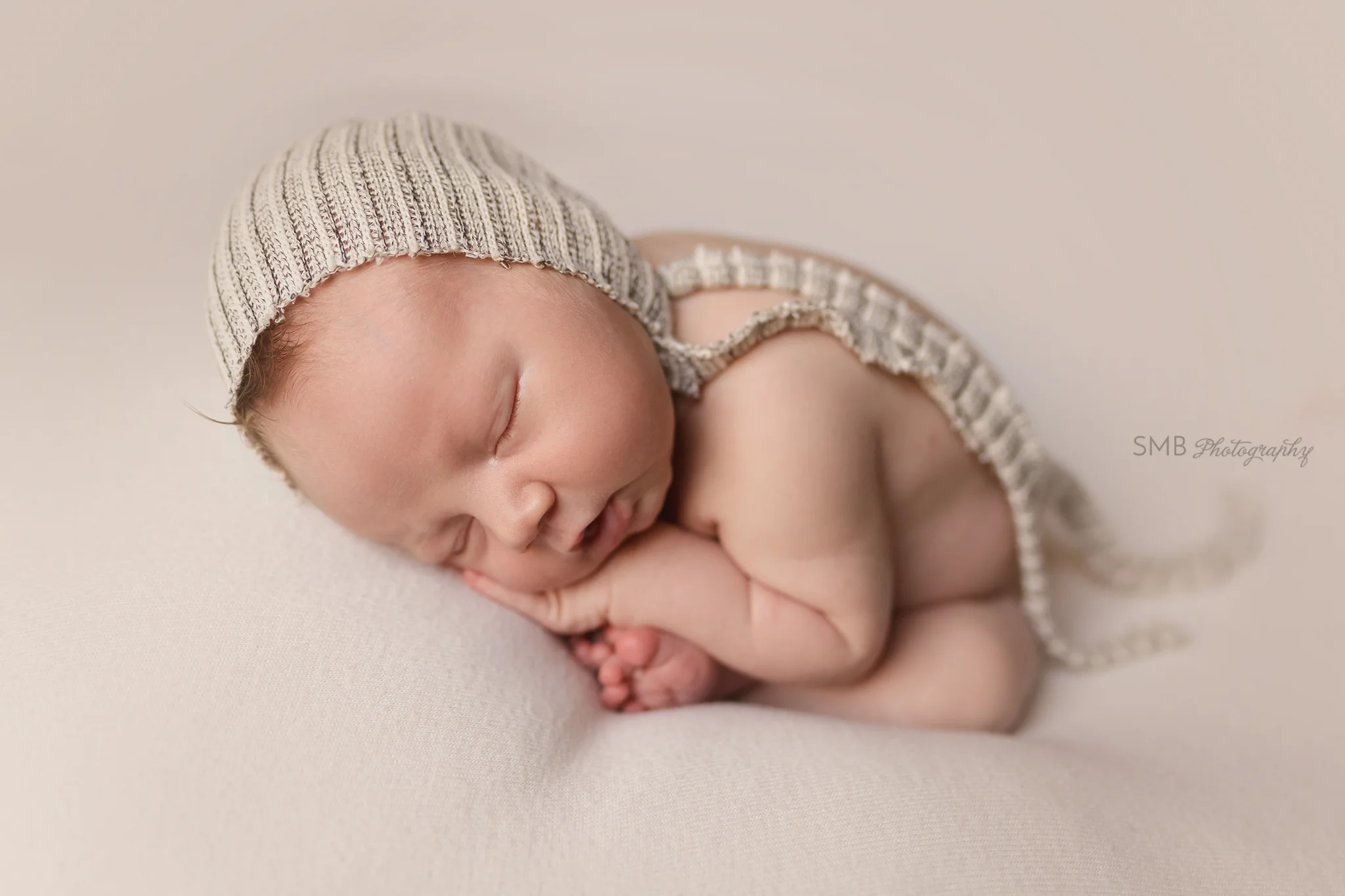 Newborn boy on cream blanket wearing stripped bonnet