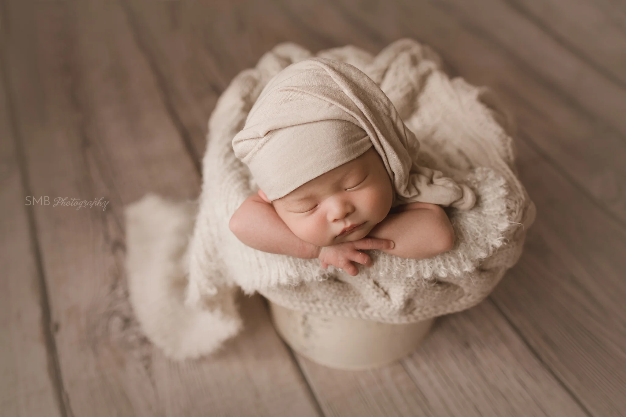 Newborn boy wearing sleepy cap in cream bucket