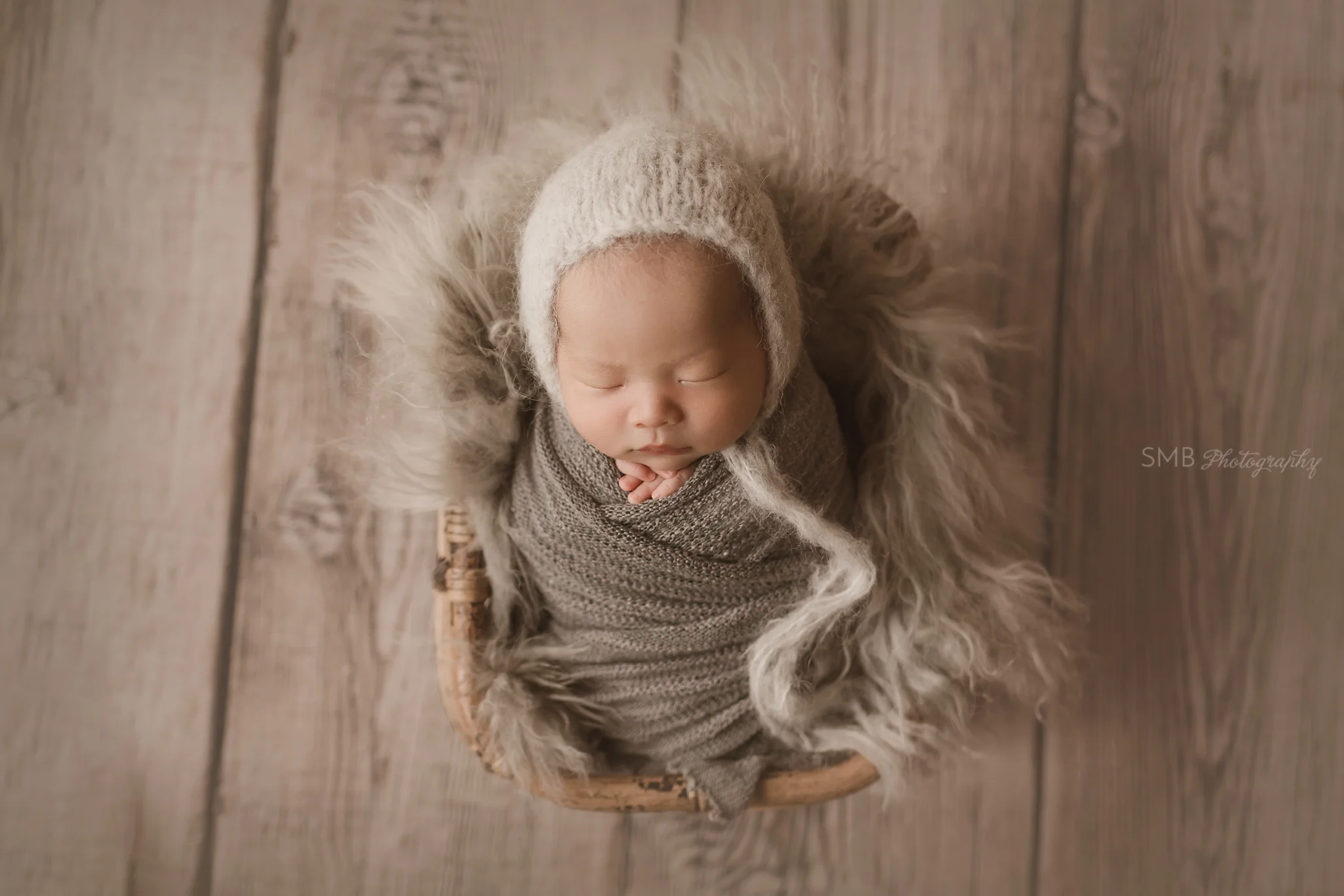 Newborn sleeping in basket on wood floor