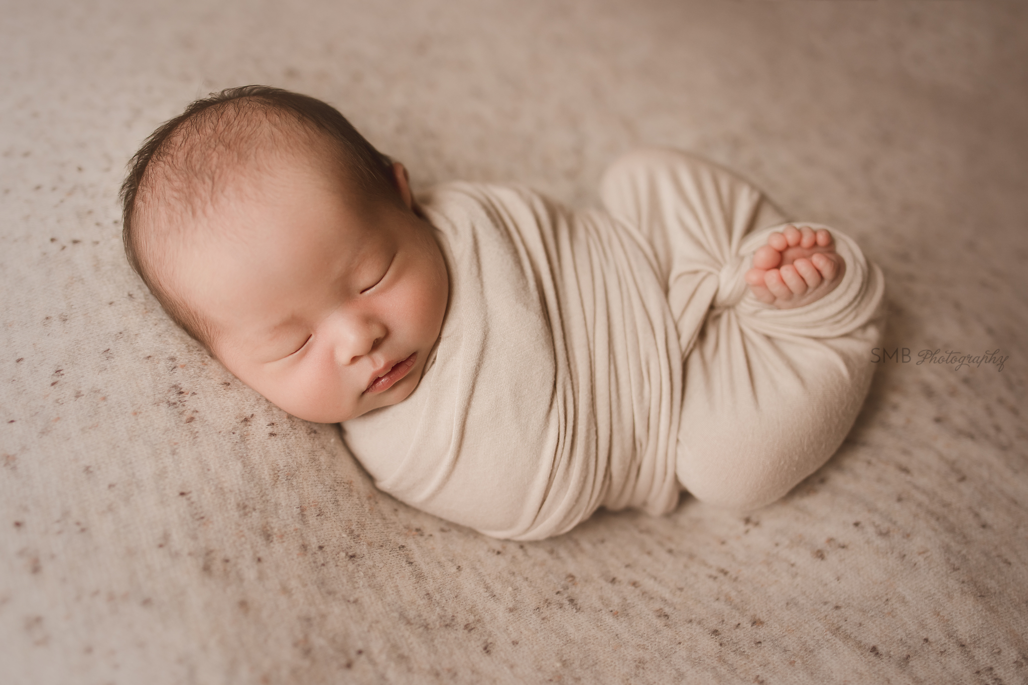 Newborn wrapped with toes out on speckled backdrop