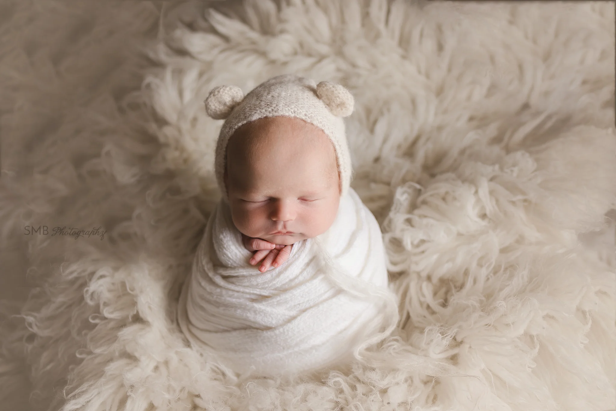 Newborn boy wrapped on cream flokati