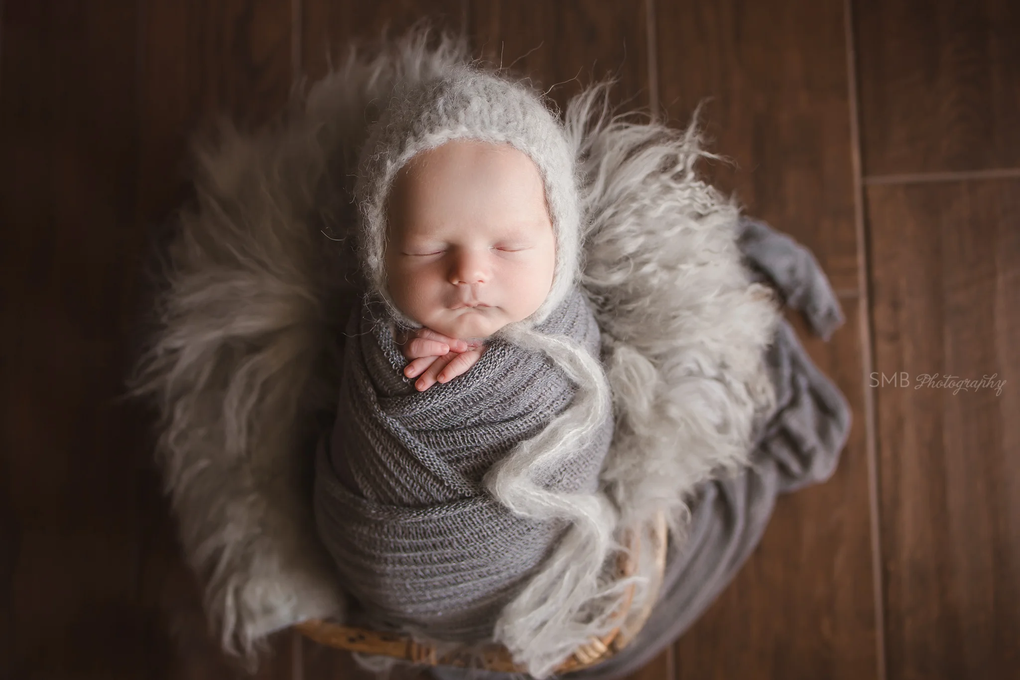Baby boy wrapped in basket on wood floor