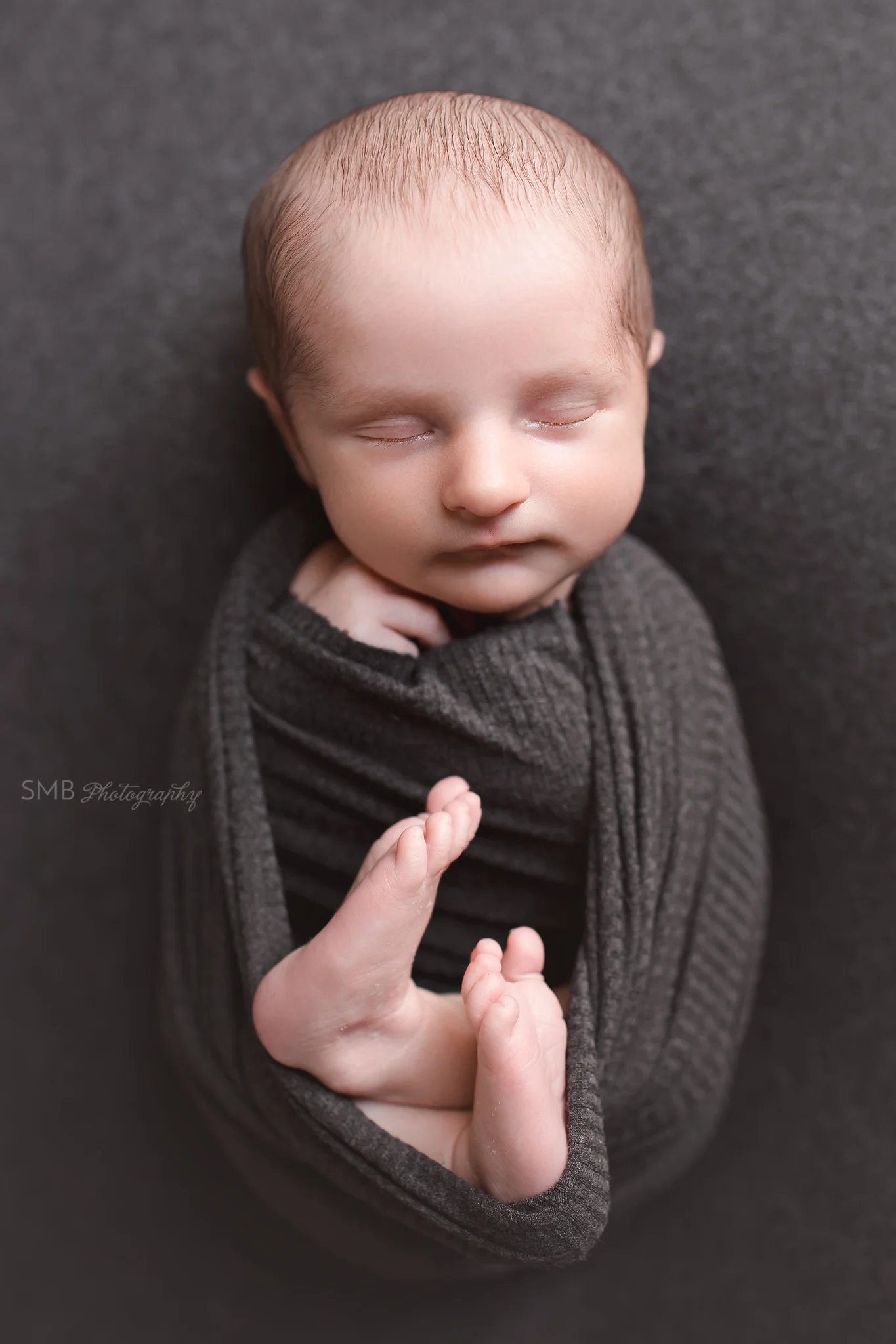 Newborn baby boy wrapped on dark gray fabric