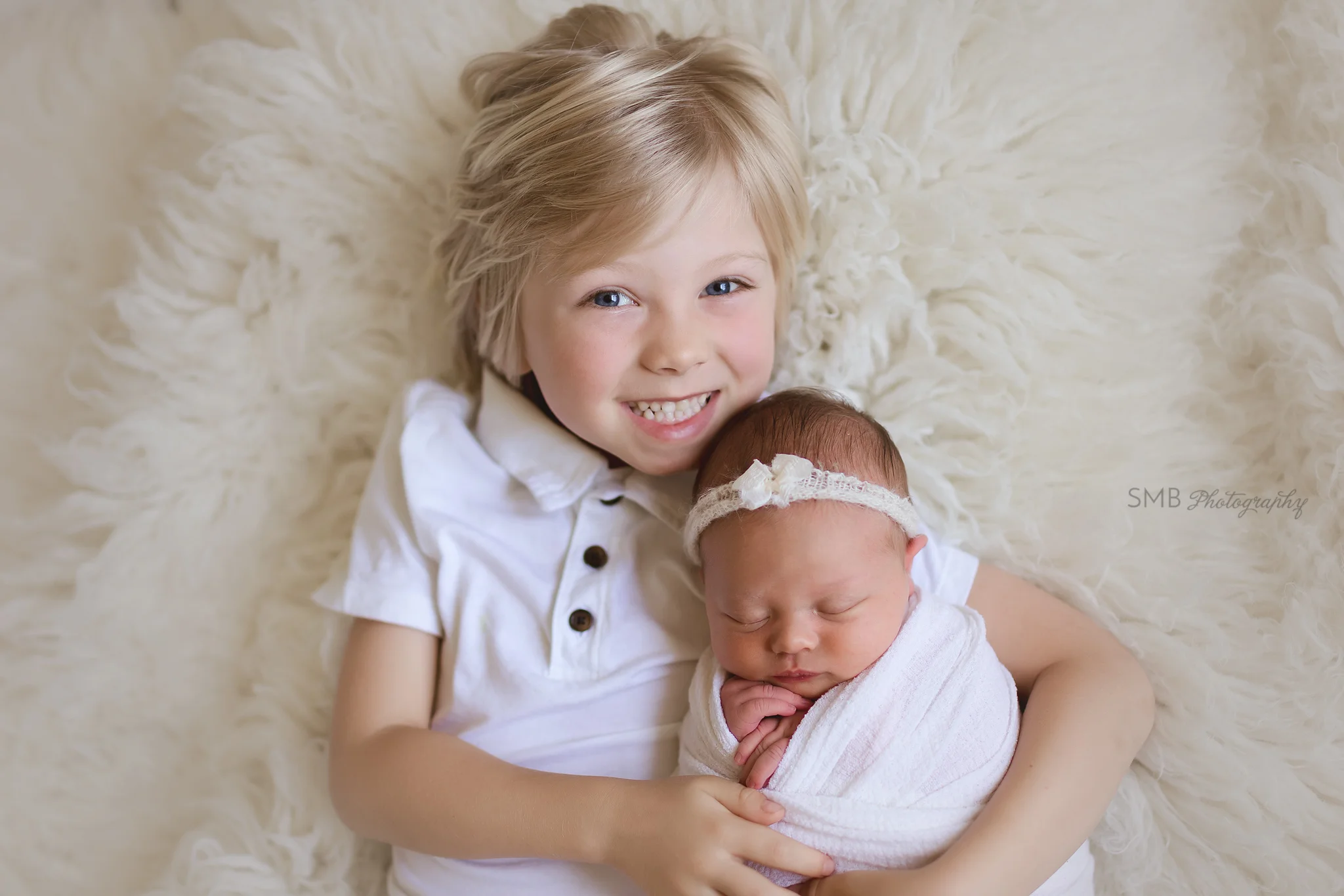 Big brother and baby sister laying on white flokati