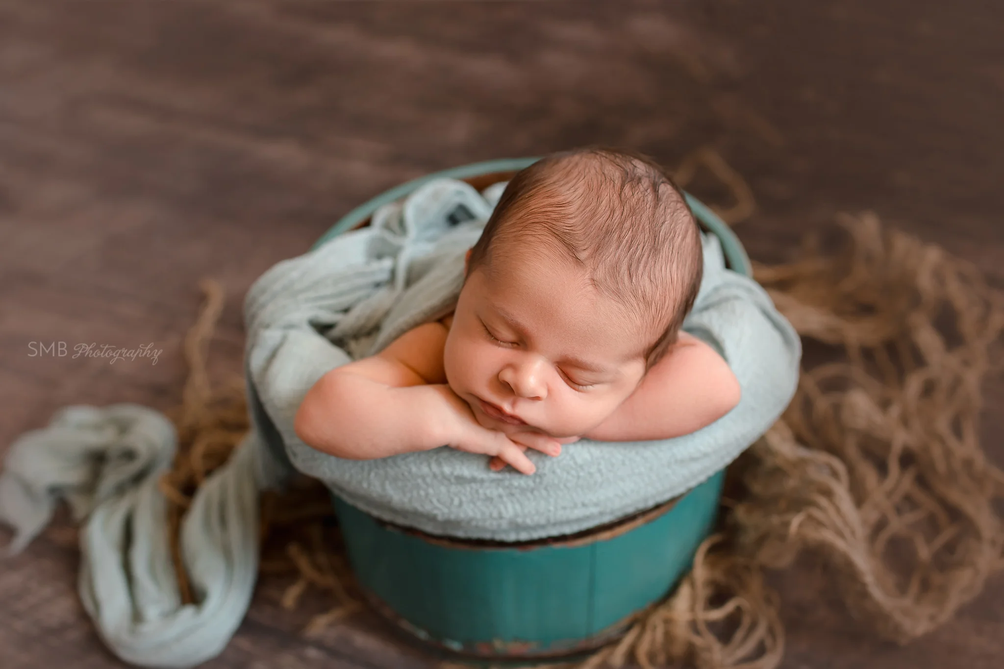 Newborn with head on hands in wood bucket