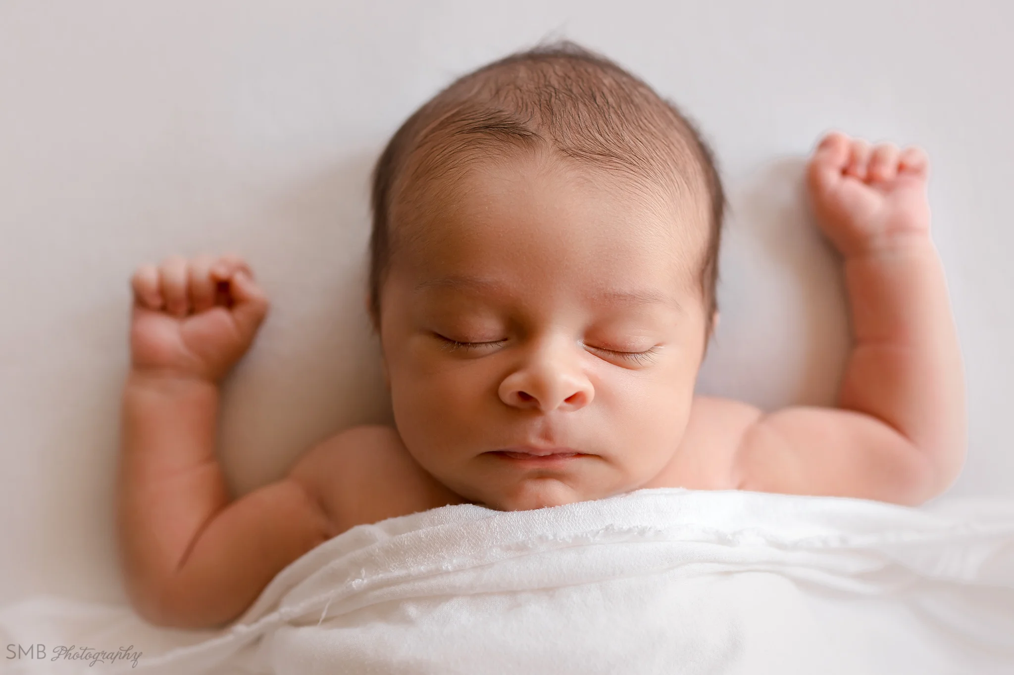 Newborn sleeping tucked in with relaxed arms and hands