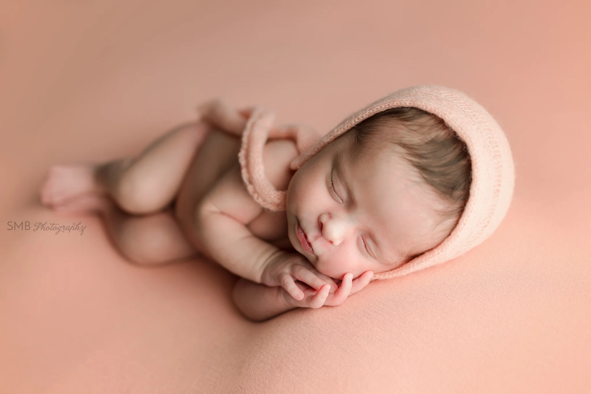 Newborn baby girl on peach backdrop wearing peach bonnet