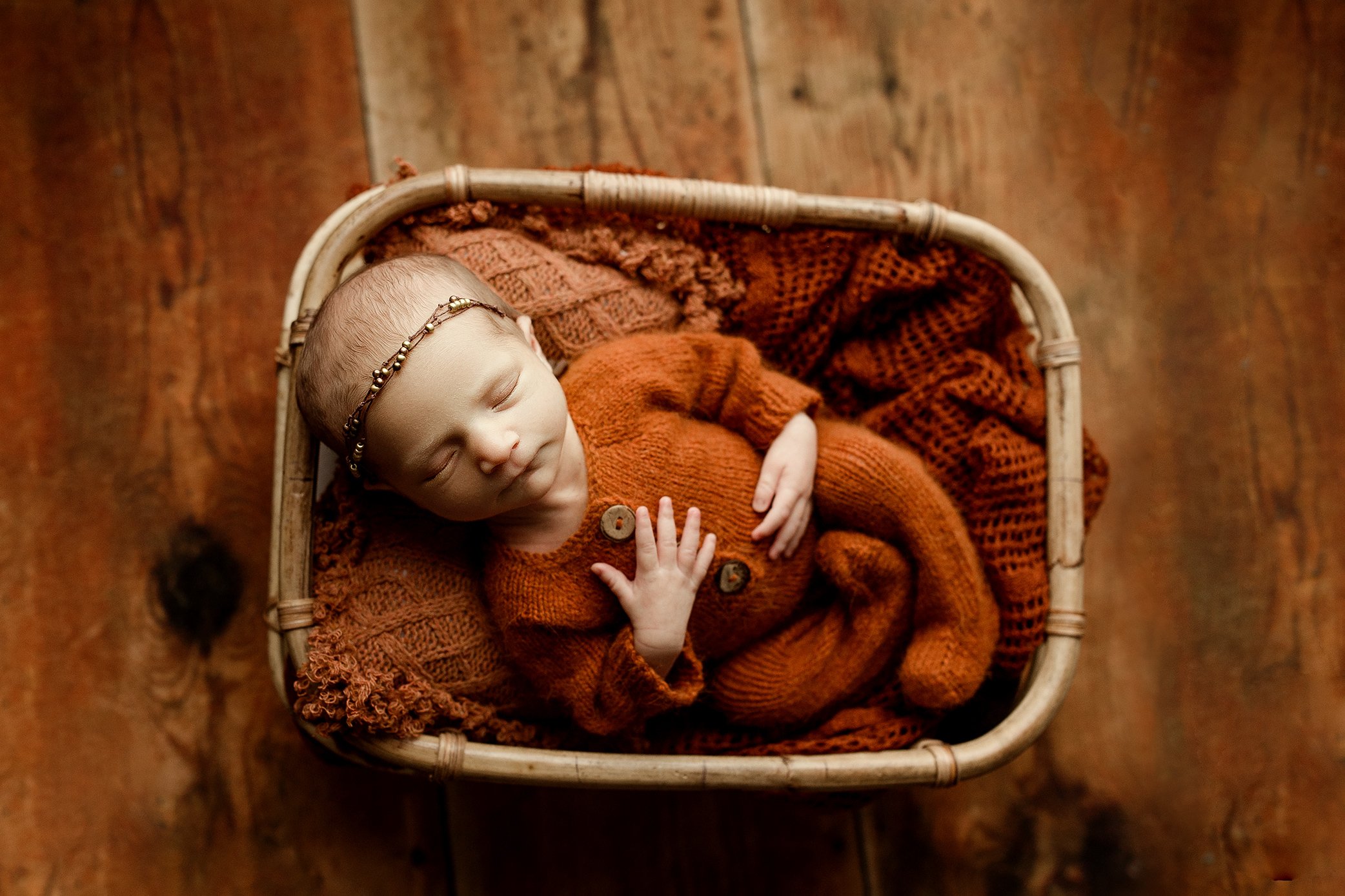 Newborn girl wearing rust colored outfit in basket