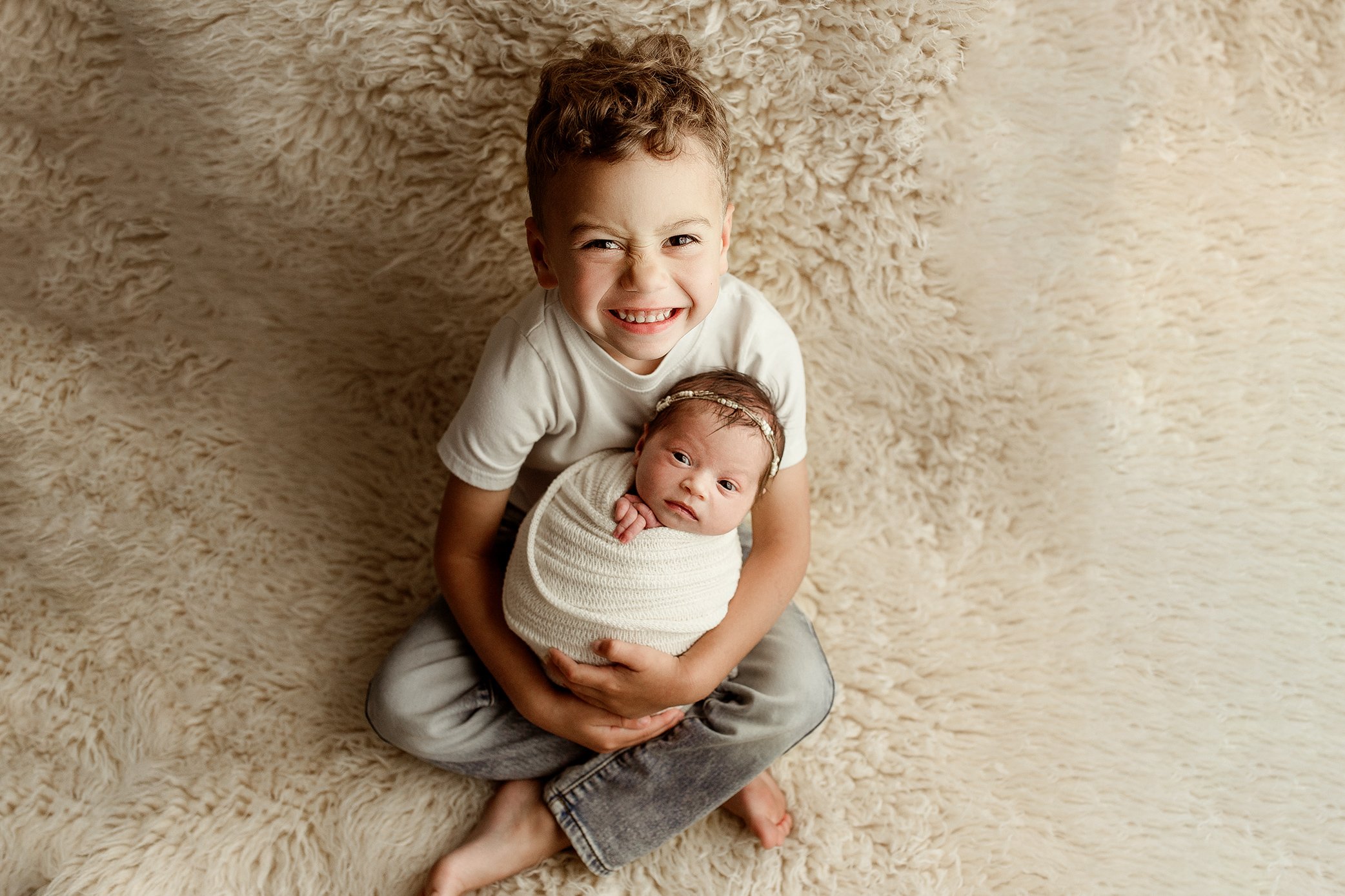 Big brother holding newborn sister smiling