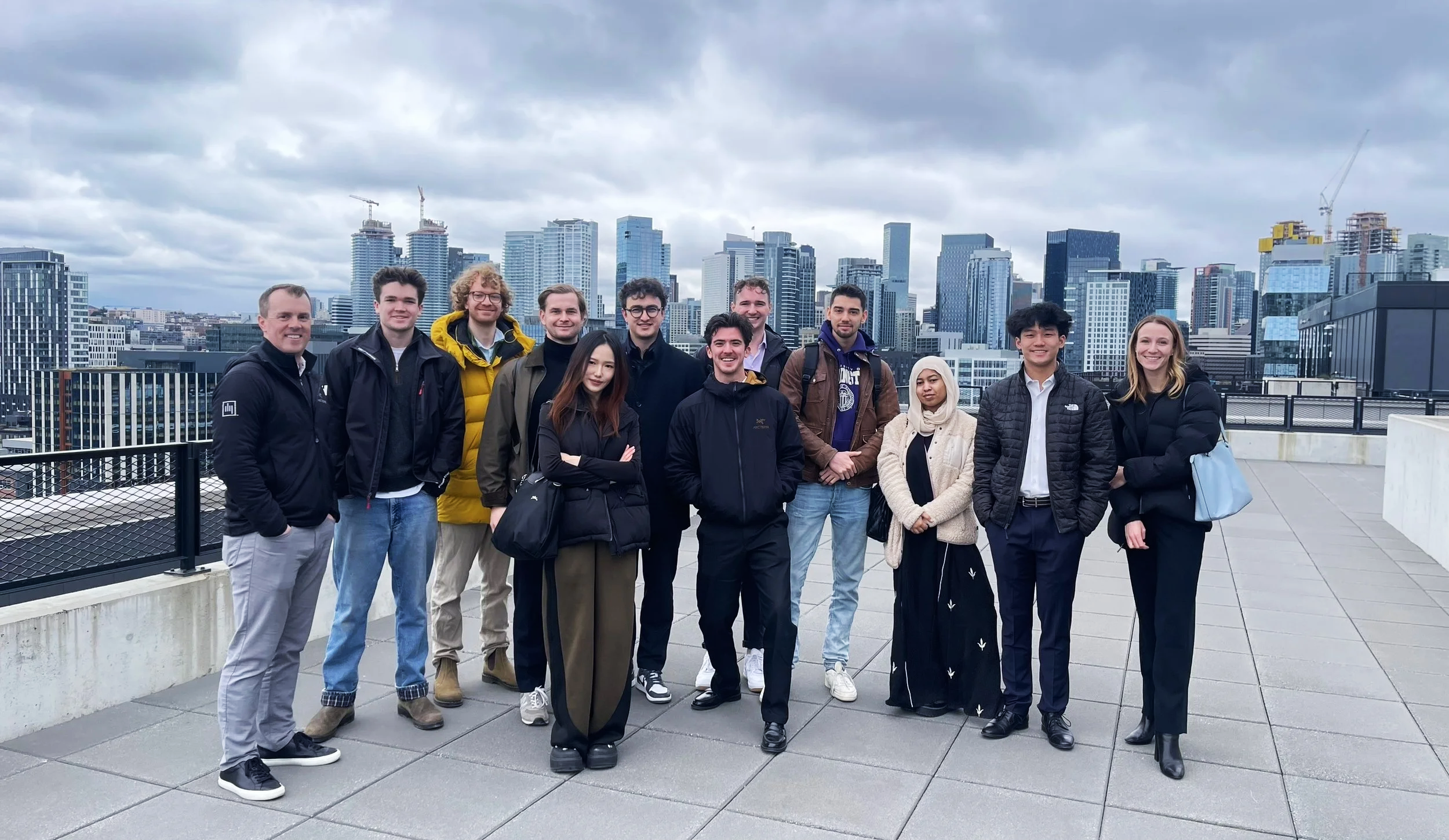 Group of diverse people posing together on a rooftop with a city skyline in the background, under cloudy skies.