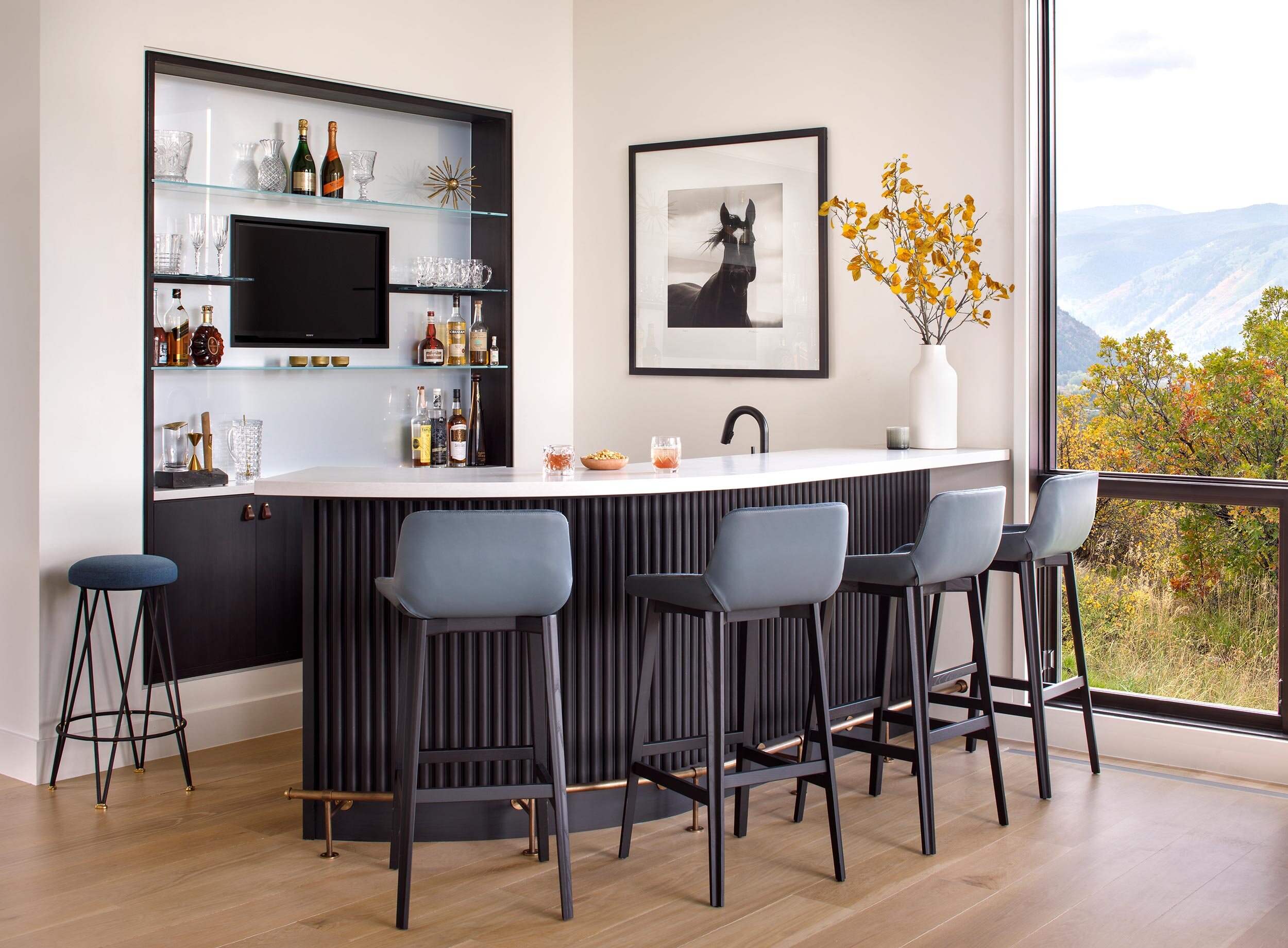 Curved black bar with blue bar stools and glass shelving in a modern Aspen chalet designed by Joe McGuire Design