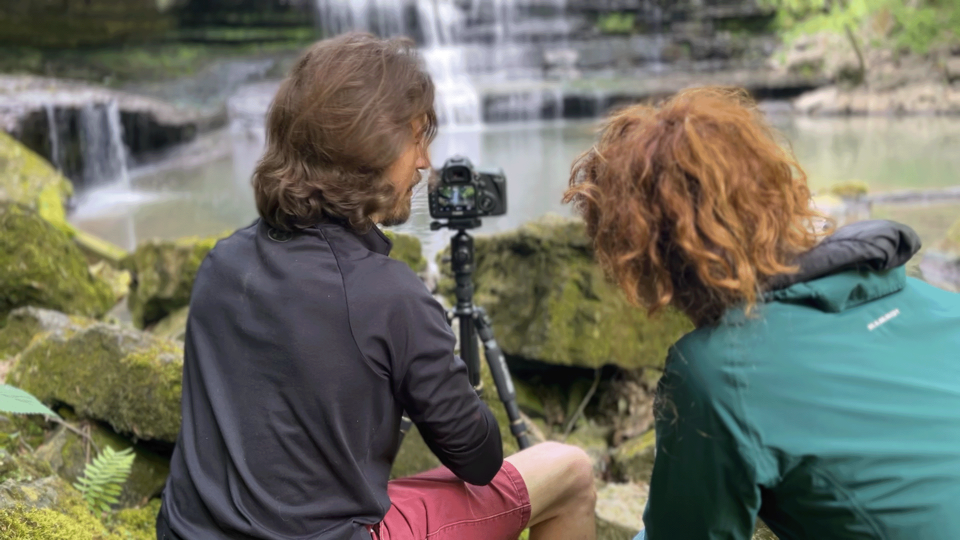 Adam Stagner teaching a workshop participant beside a waterfall with a tripod-mounted camera