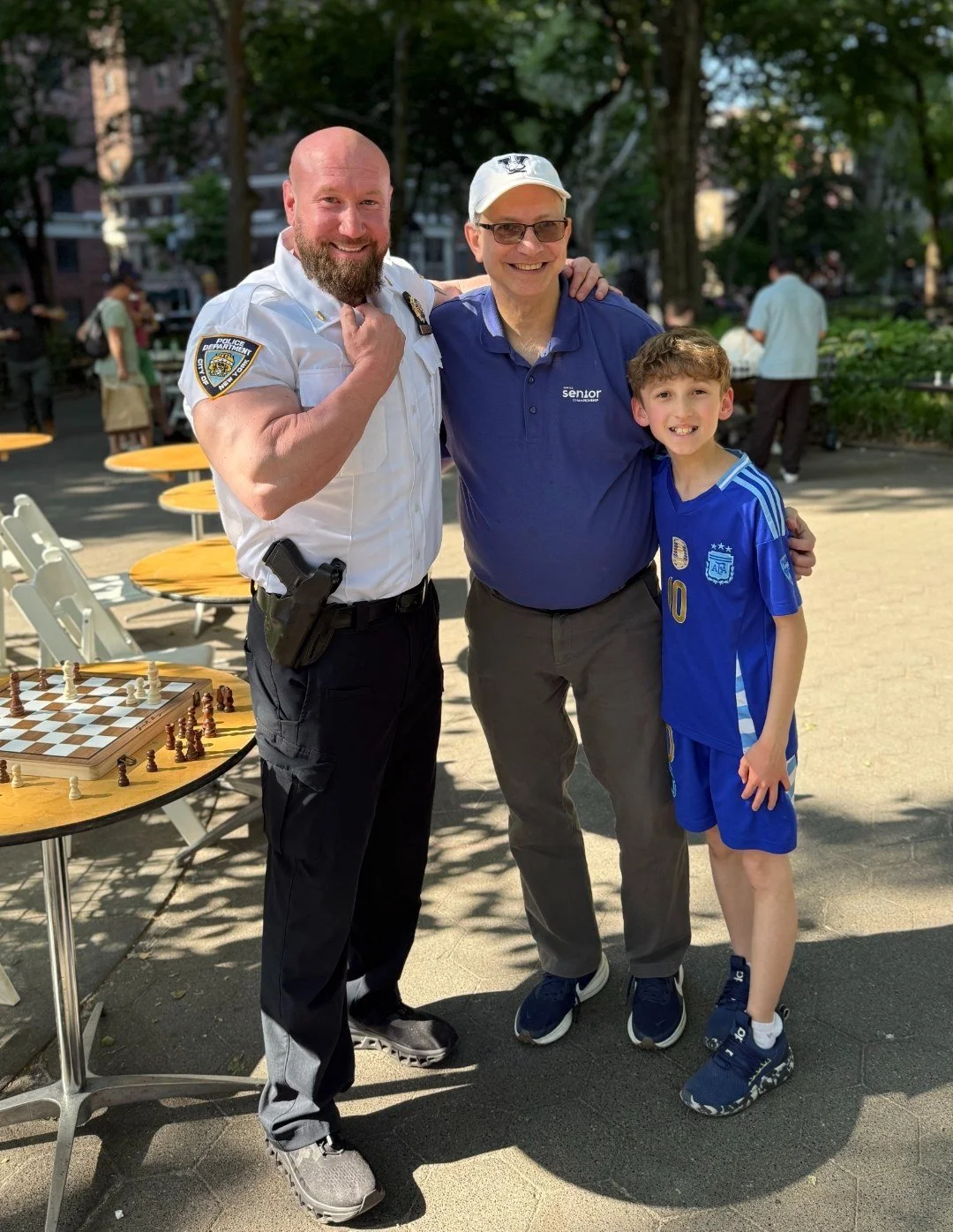 From left to right: Lieutenant Darin Lazar, Grandmaster Joel Benjamin, and Hudson Lazar smiling next to a chess board