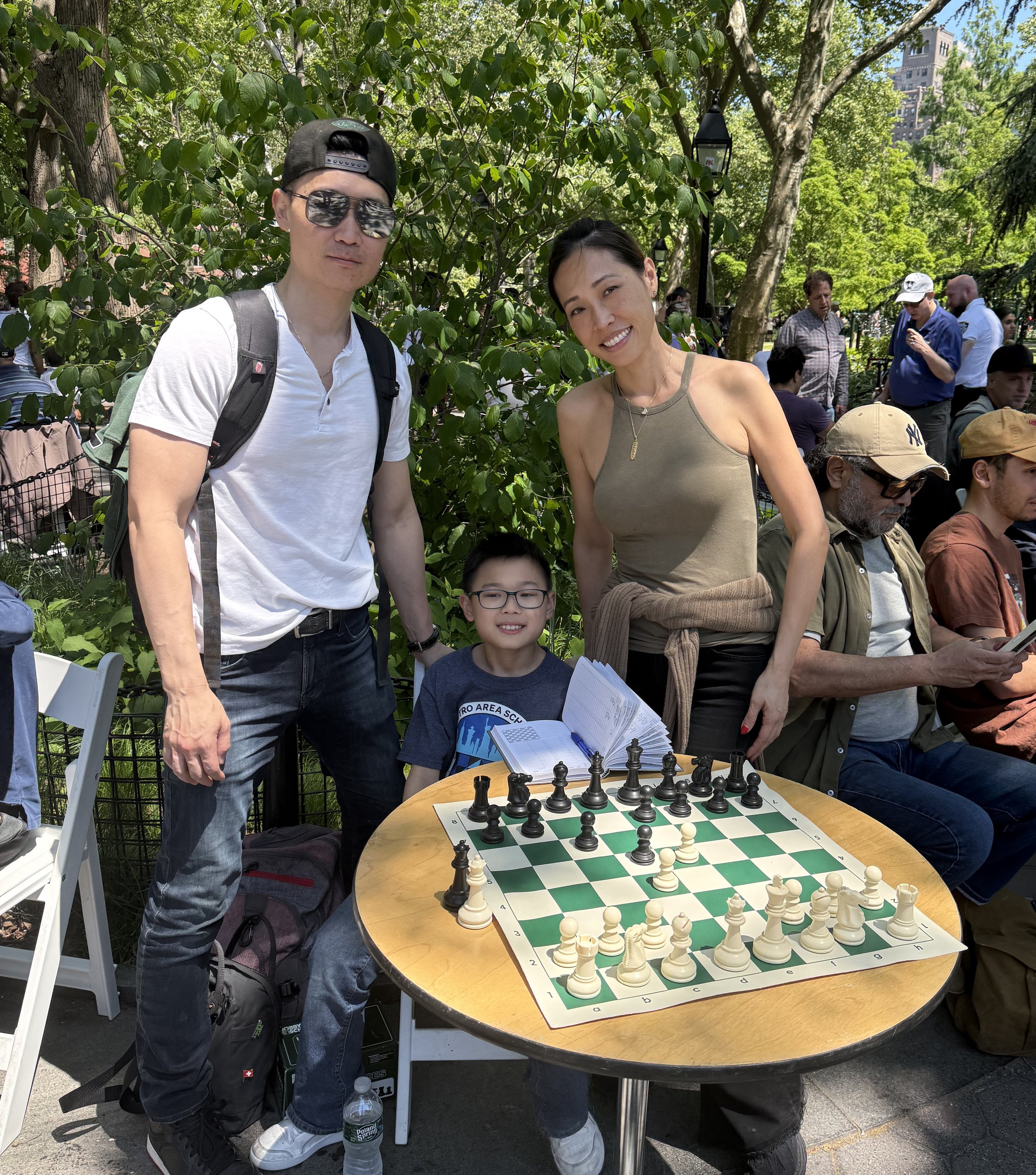 Brendan Seto sits at his chess table with father Tony Seto standing behind him to the left and his mother, Grace Chen-Seto, standing to the right