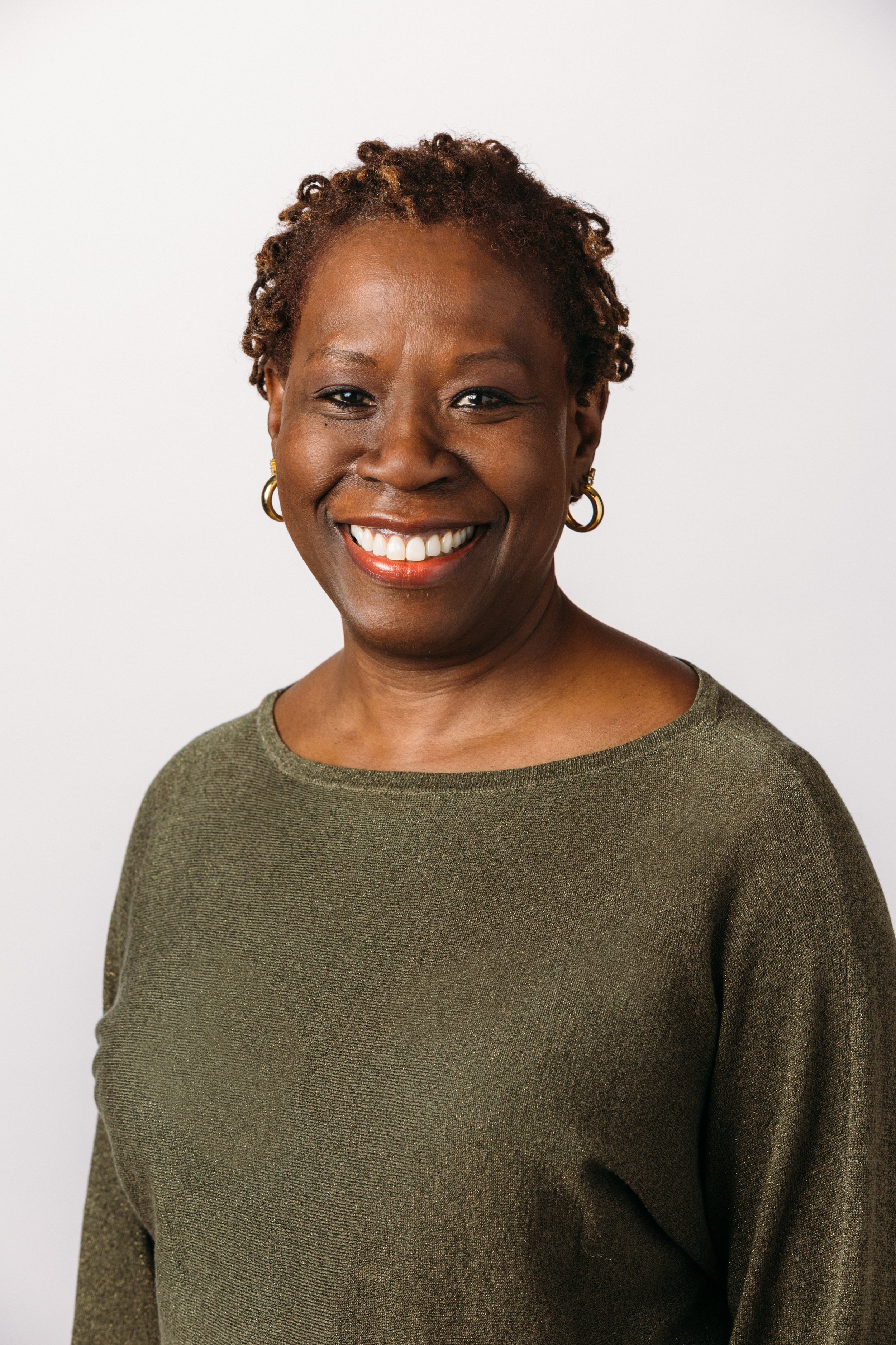A Black woman with short orange brown hair, wearing an olive green shirt, smiling at the camera.