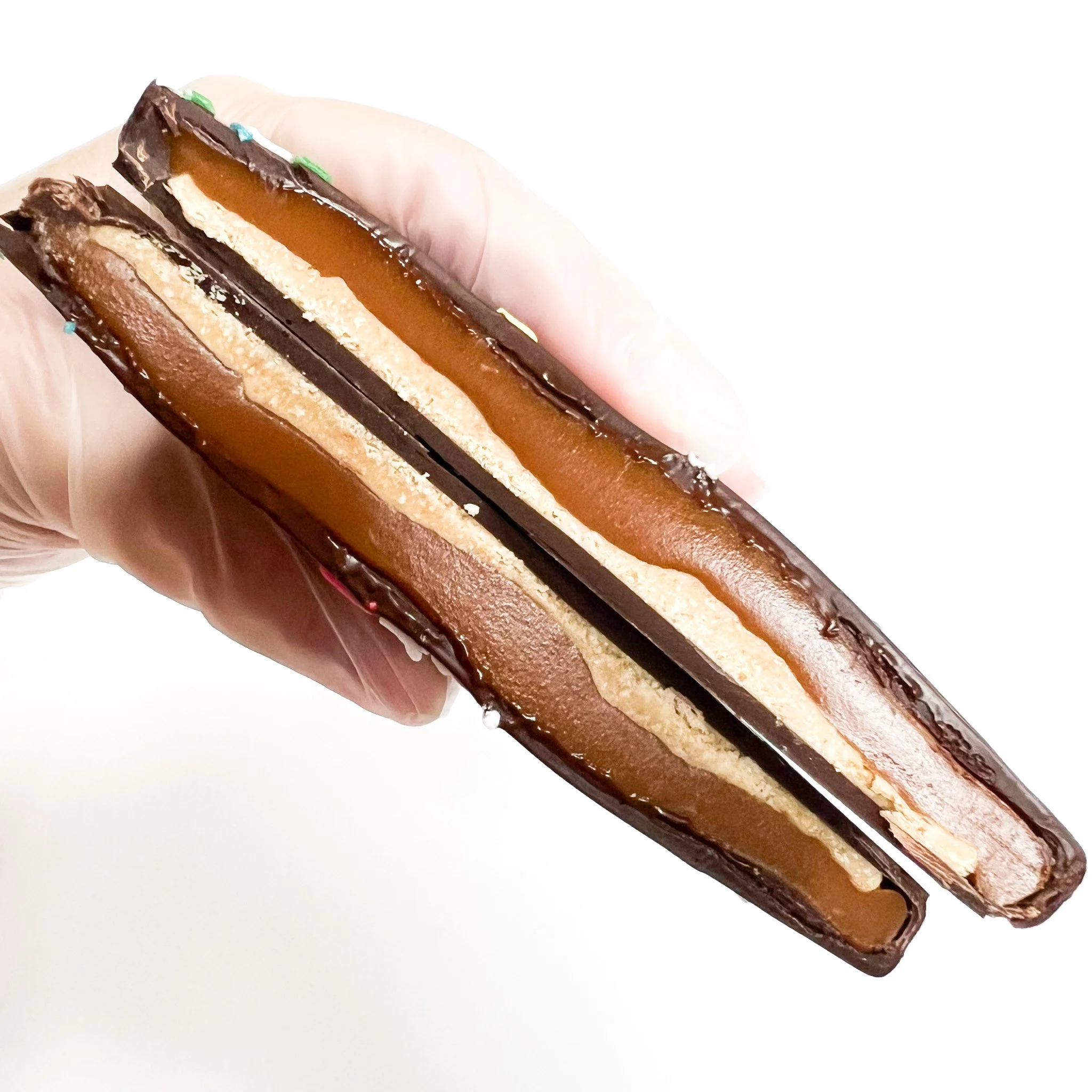 Close-up of a chocolate and caramel layered dessert bar held in a person's hand.