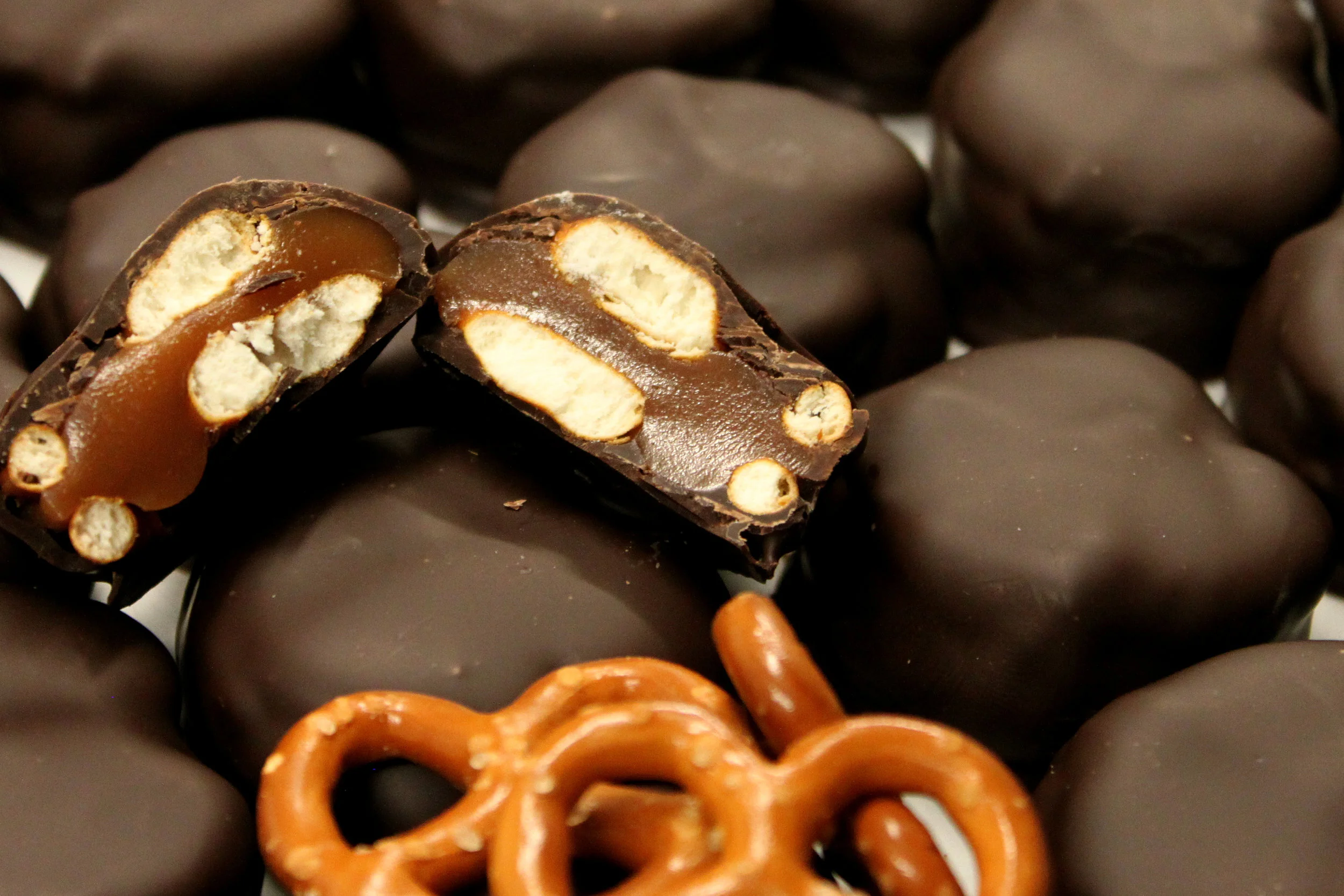 Close-up of assorted chocolates, including whole and halved pieces showing caramel, biscuit, and nougat fillings, with some pretzels at the bottom.