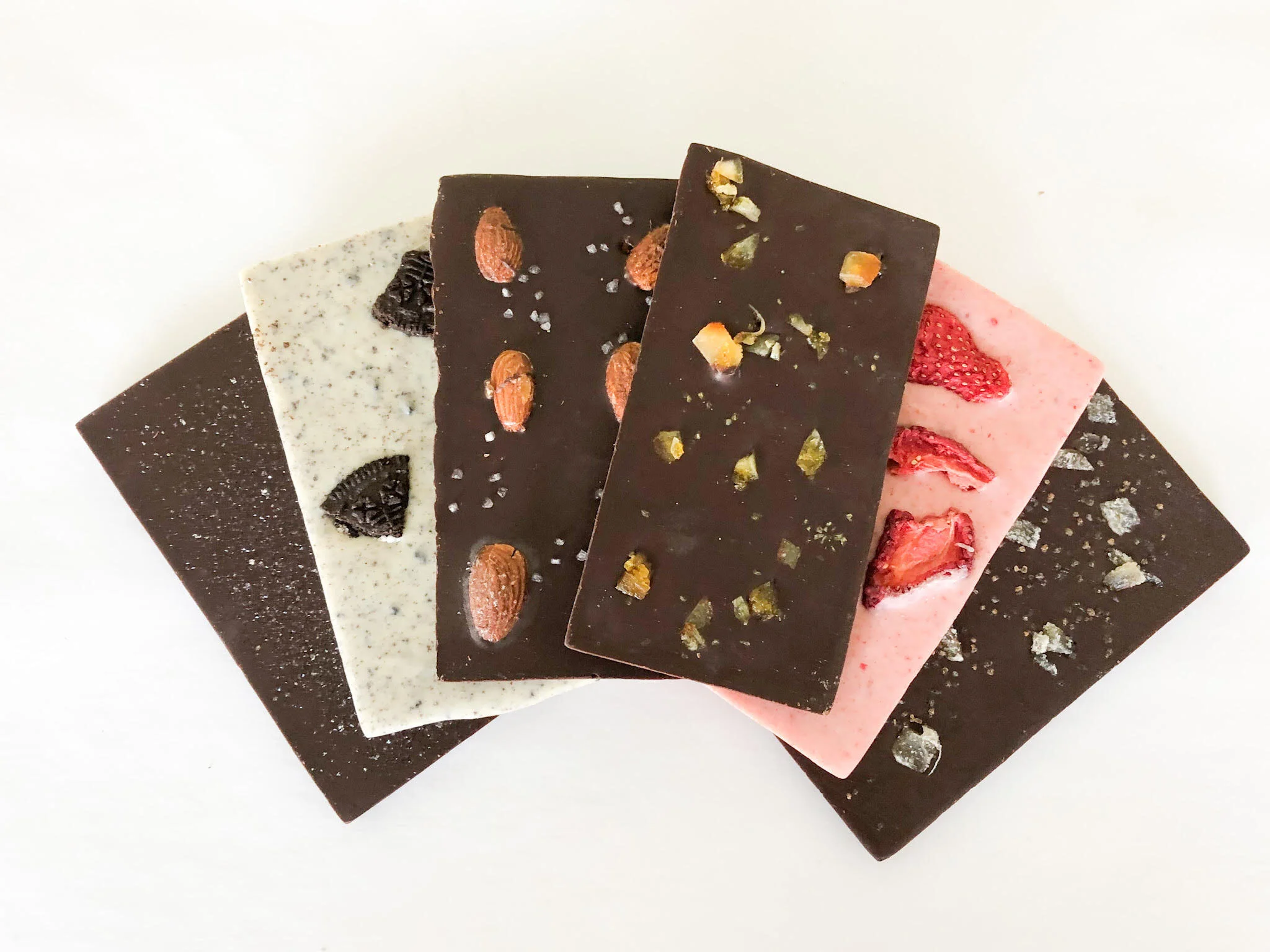 Close-up of assorted flavored chocolate bars with various toppings, arranged on a white surface.