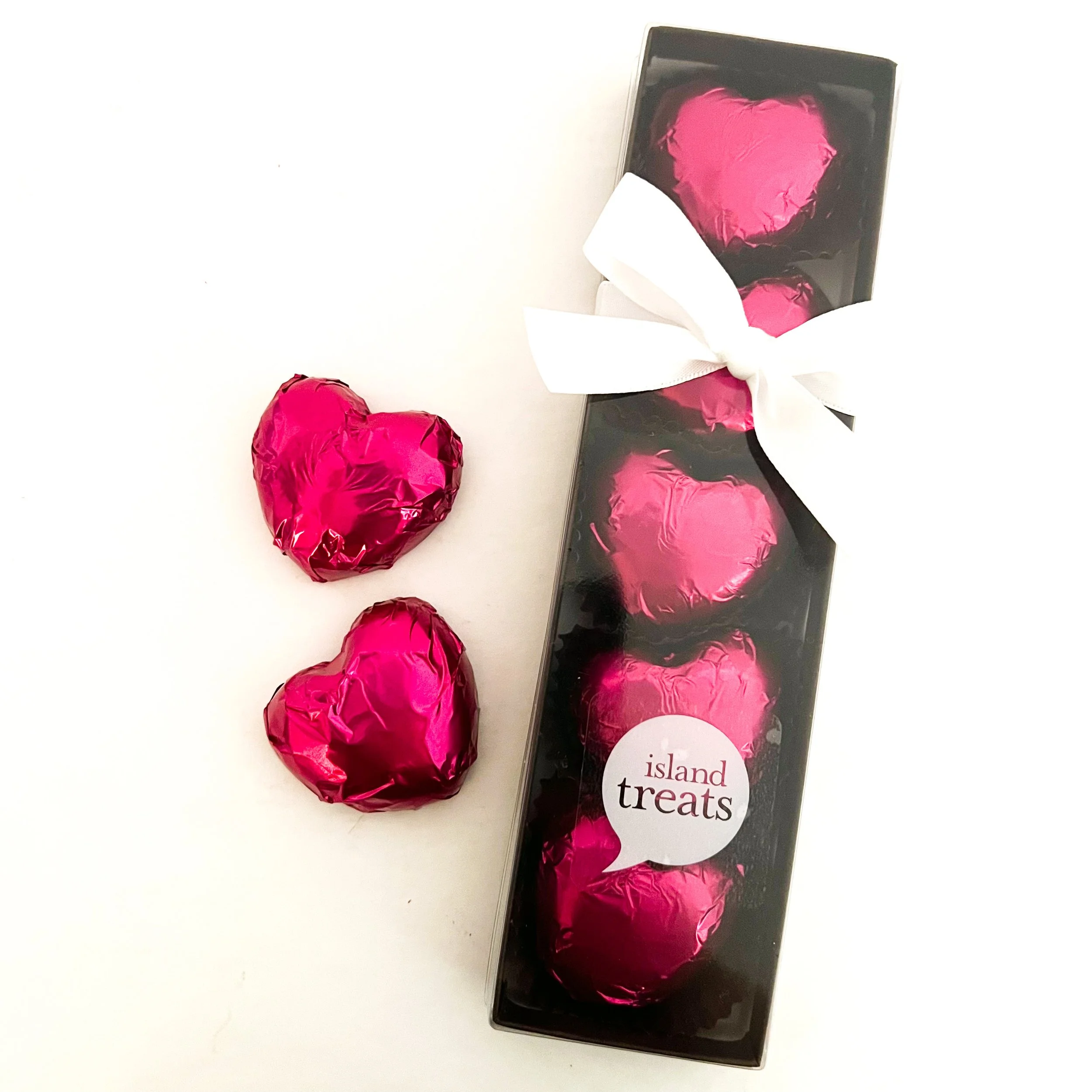 Decorative chocolates wrapped in pink foil alongside a black box with a heart-shaped artwork and the text 'island treats' on a white background.