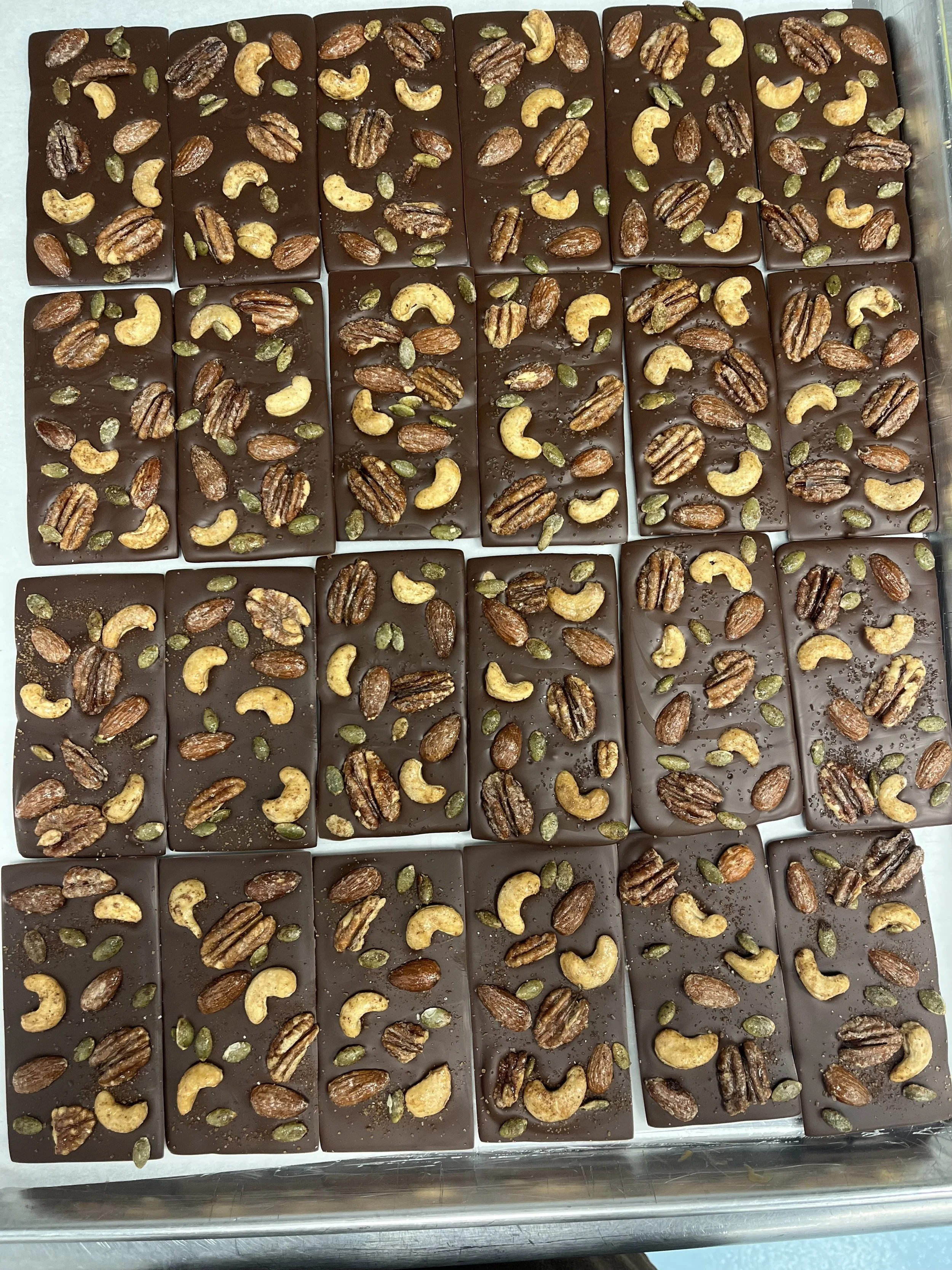 Handcrafted chocolate bars from a Seattle chocolate maker, topped with roasted nuts and seeds and arranged in a production tray.