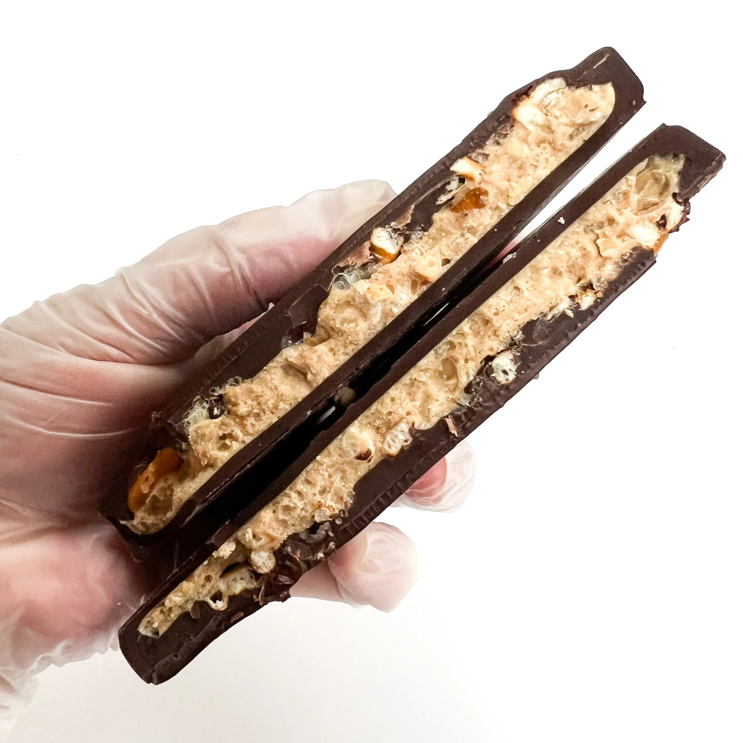 Close-up of a chocolate coated wafer snack with nuts, held in a gloved hand against a white background.